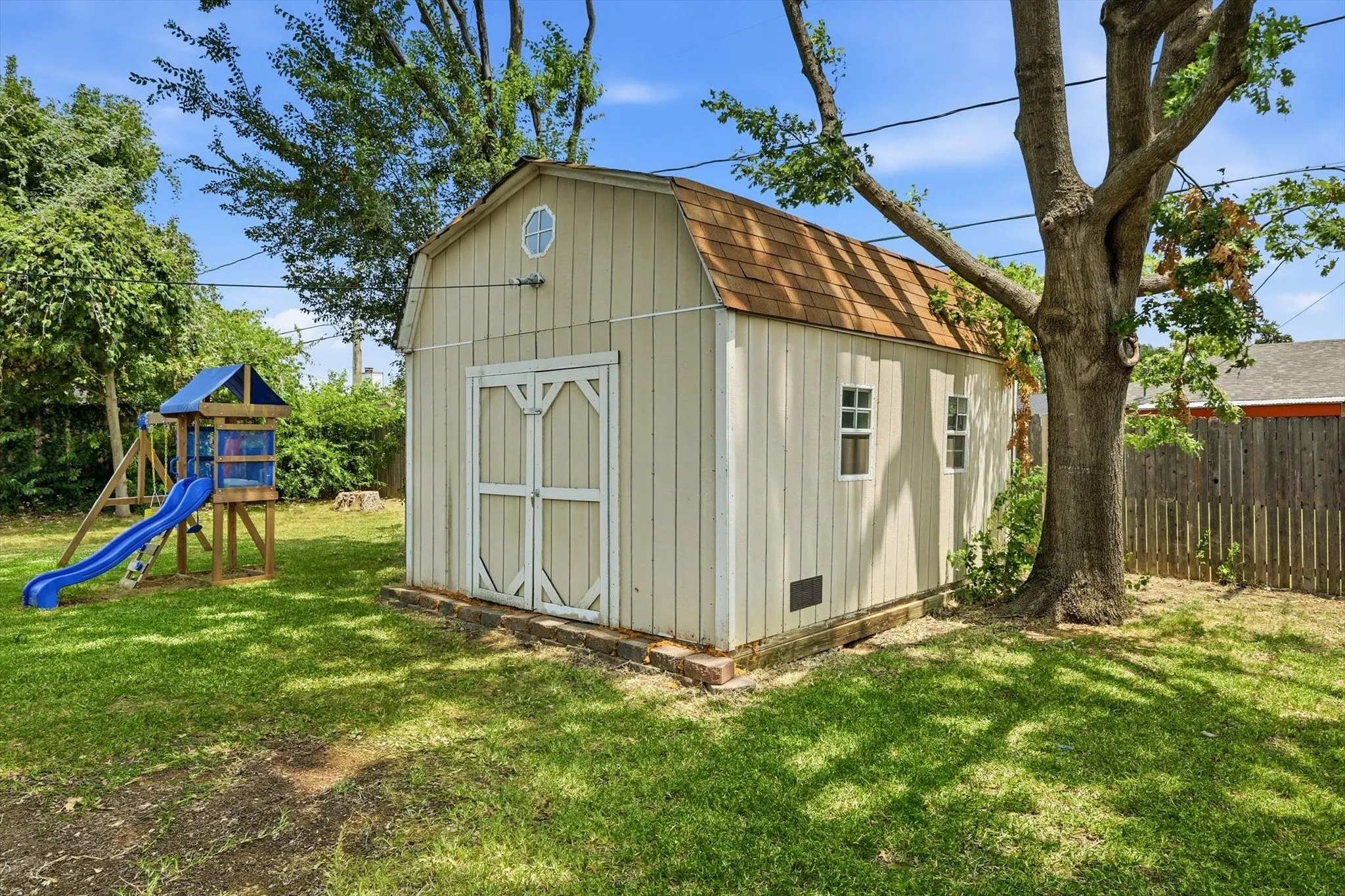 Backyard featuring a wooden storage shed with a gambrel roof, double entry doors, two side windows, and an oval window on the gable end