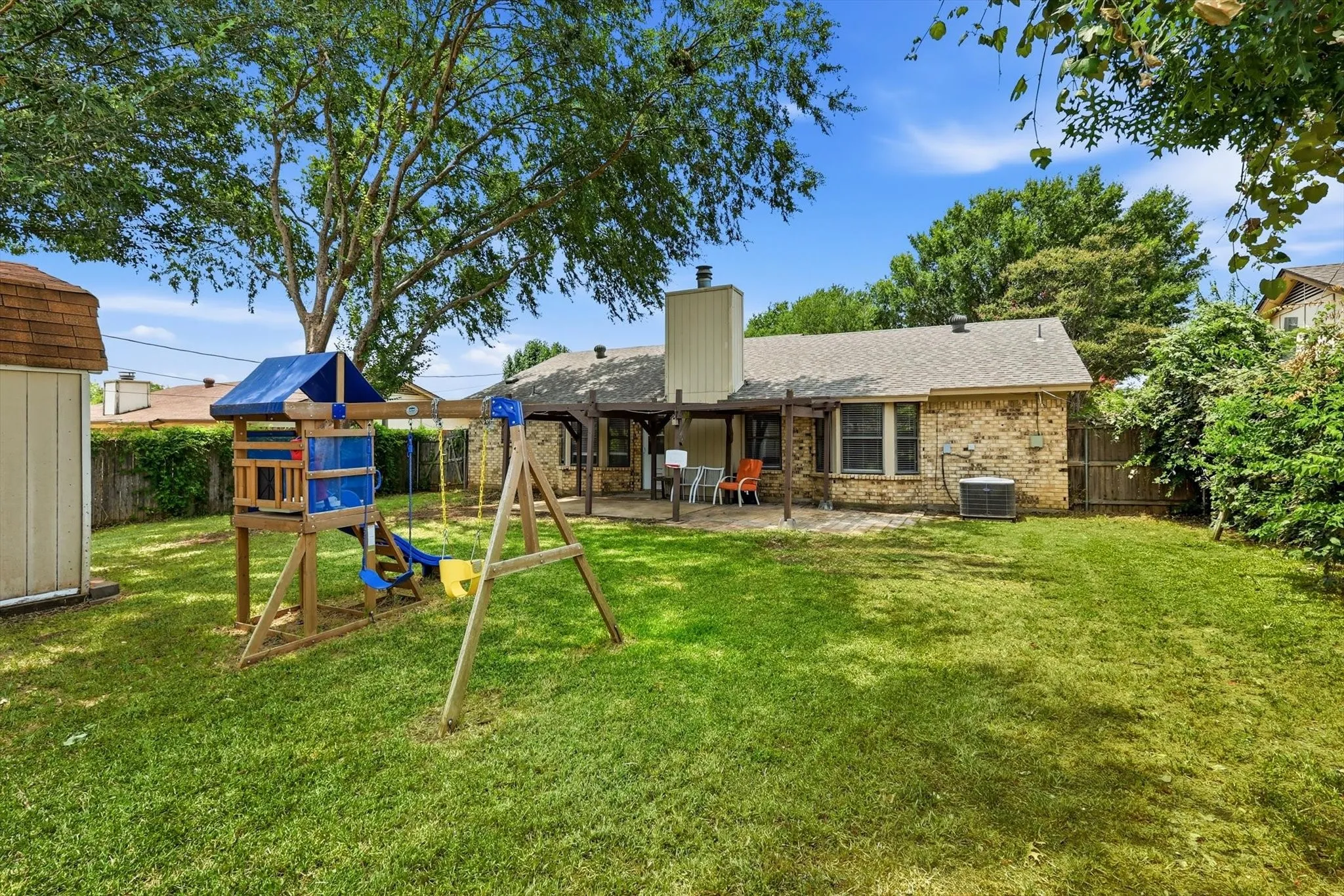 Expansive backyard featuring a large tree, a detached storage shed, and a stone-paved patio with an attached pergola