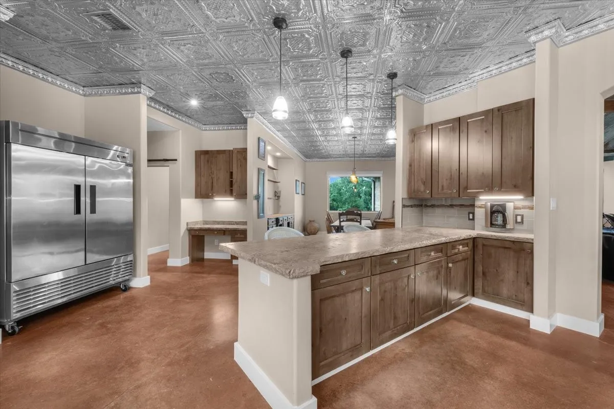 Kitchen featuring a tin-tile ceiling, wood-finish cabinetry, a large kitchen island with a stone-finish countertop, and polished concrete flooring