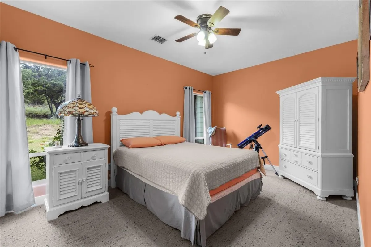 Bedroom featuring a window with exterior tree-line scenery, light-toned carpet flooring, and a ceiling fan with integrated lighting