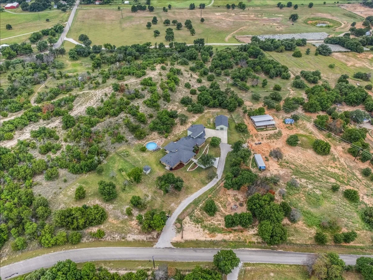 Expansive property featuring a winding driveway, a main residence with a dark roof, a round above-ground pool, and multiple outbuildings