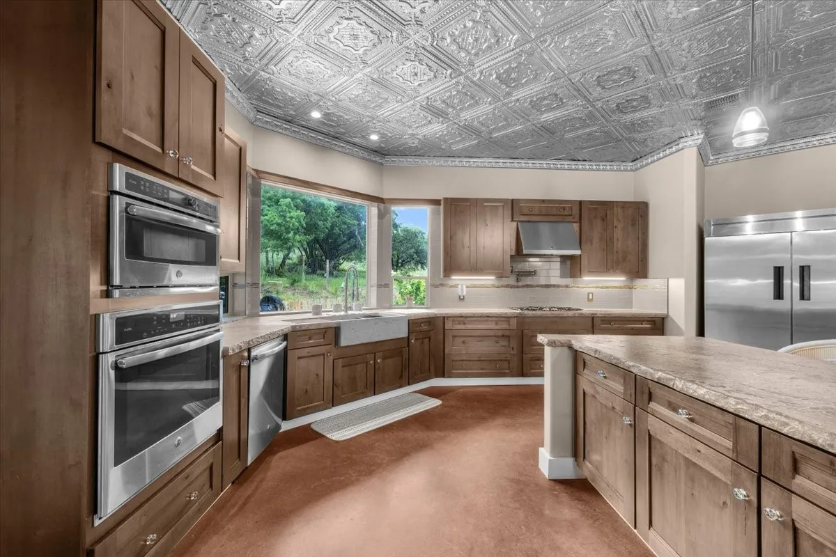 Kitchen featuring a decorative tin ceiling, wood cabinetry, built-in stainless steel double ovens, a farmhouse sink, and polished countertops