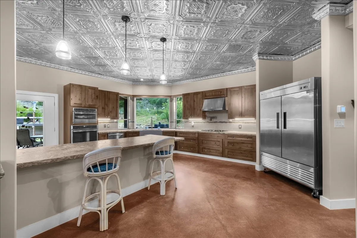 Kitchen featuring a patterned ceiling, wood-finish cabinetry, stainless steel appliances, a bay window, and a peninsula with a stone-finish countertop