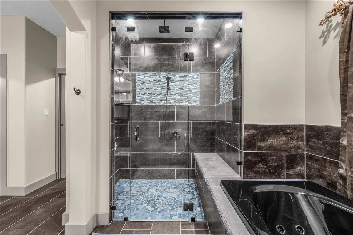 Glass-enclosed shower featuring dark-toned large format tiles, pebble-style flooring, a mosaic accent band, and a built-in bench