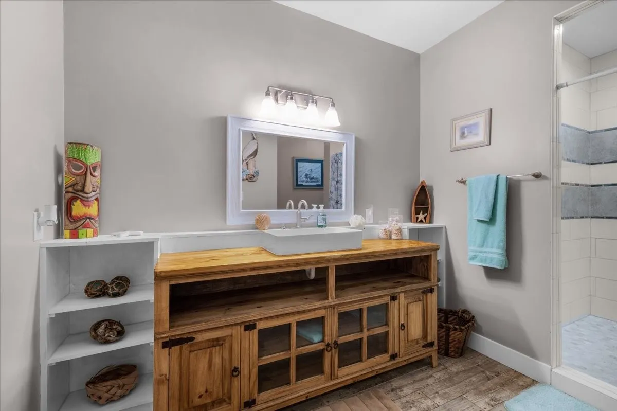 Bathroom featuring a custom wood vanity with a vessel sink, a framed mirror with integrated lighting, and a shower with tiled walls and a glass enclosure