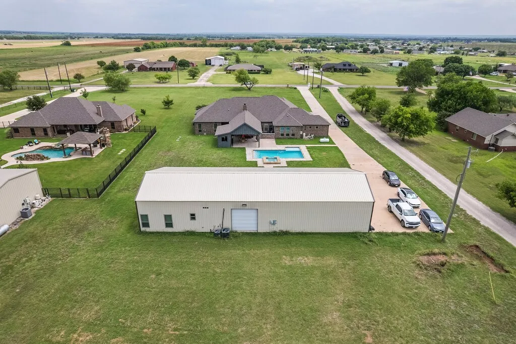 Expansive property featuring a large metal outbuilding, a rectangular swimming pool, and a gravel driveway