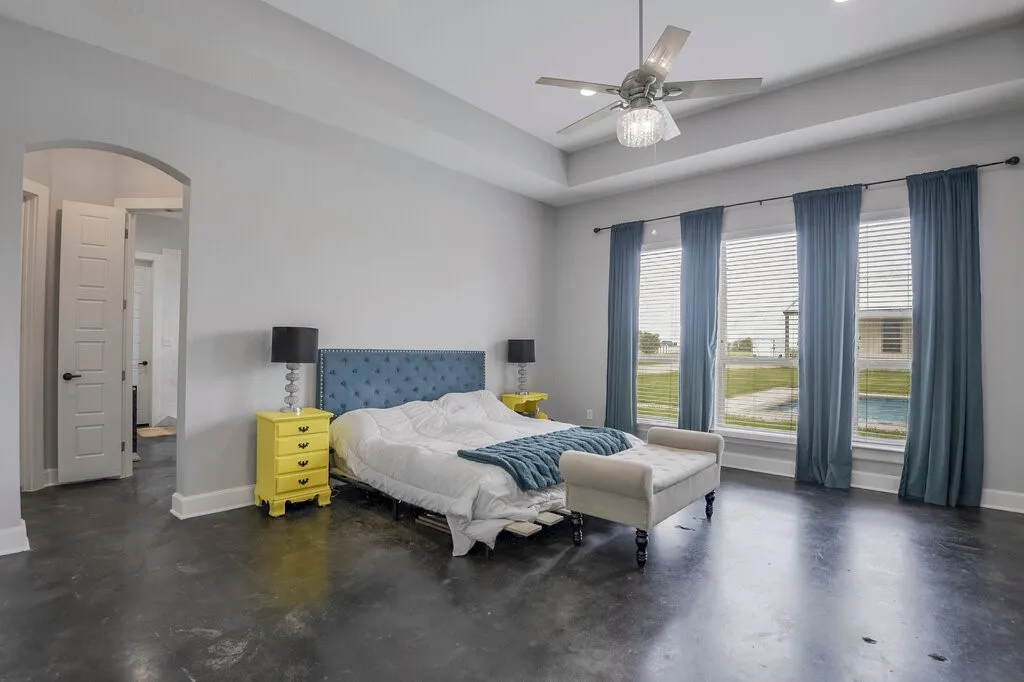 Spacious room featuring concrete-finish flooring, a tray ceiling, and a ceiling fan with integrated lighting