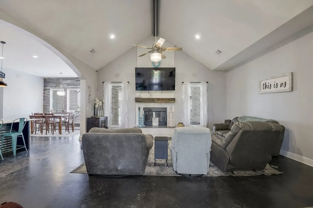 Vaulted ceiling living area featuring dark finish flooring, a fireplace with a wood mantle, and an arched doorway opening to a dining area with a shiplap accent wall