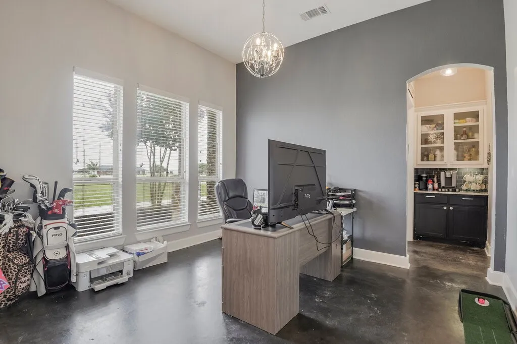 Room featuring polished concrete flooring, three large windows with horizontal blinds, a contemporary chandelier, and an arched doorway leading to a built-in cabinet area