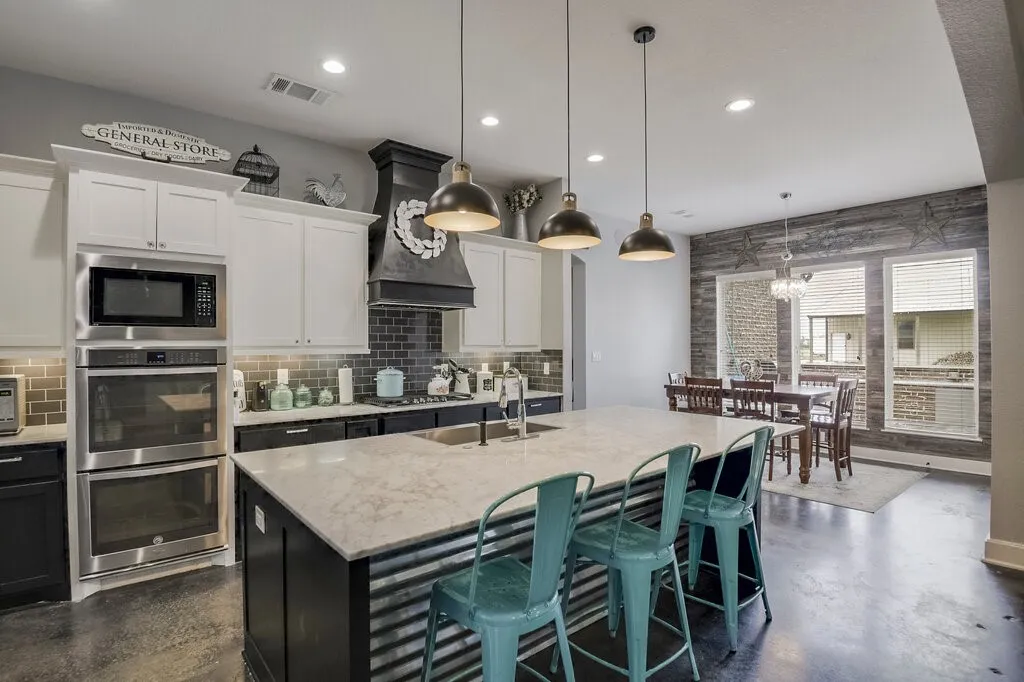 Open-concept kitchen featuring an oversized island with a light-toned countertop, pendant lighting, stainless steel double ovens, and a subway tile backsplash