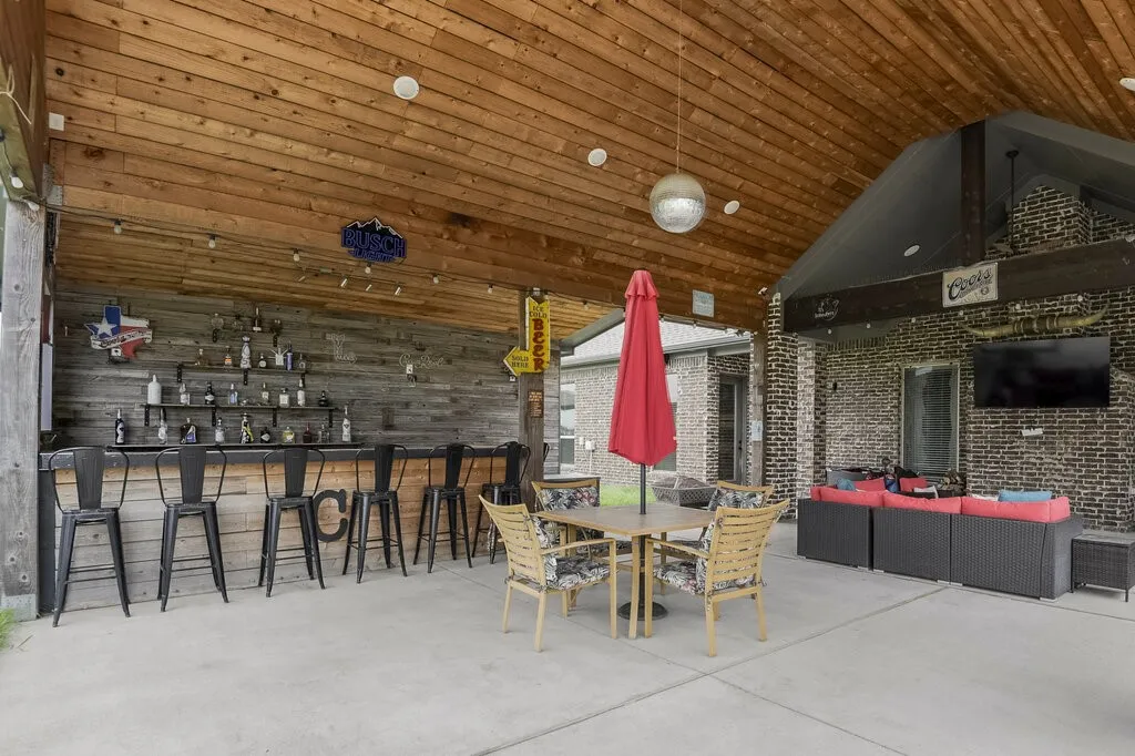 Spacious covered patio featuring a wood-plank ceiling, concrete flooring, and a built-in bar with shelving