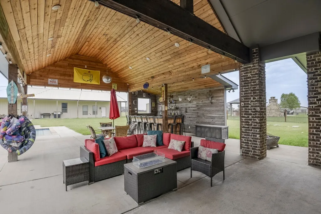 Expansive covered patio featuring a vaulted wood-plank ceiling, concrete flooring, exposed wood beams, and a built-in wet bar with a shiplap accent wall