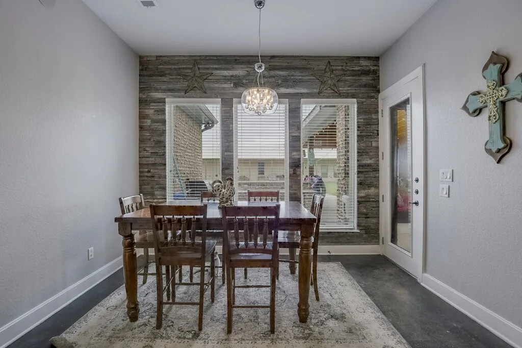 Dining area featuring a wood-look accent wall, three large windows with horizontal blinds, and a frosted glass-panel door