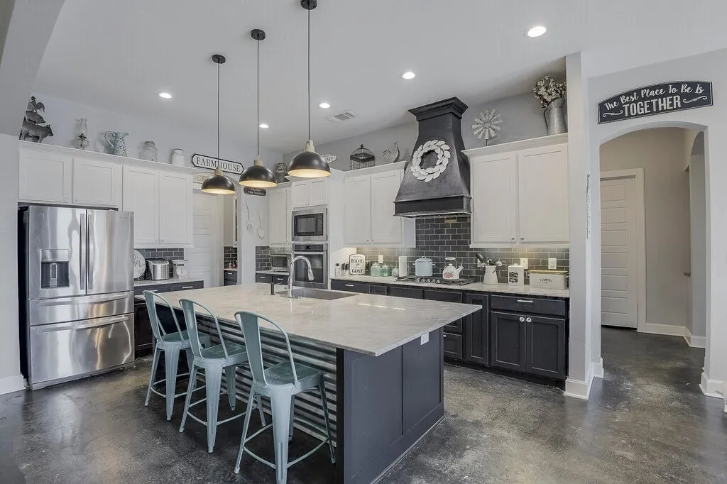 Spacious kitchen featuring a large central island with seating, a custom dark range hood, stainless steel appliances, two-tone cabinetry, and wood-finish flooring