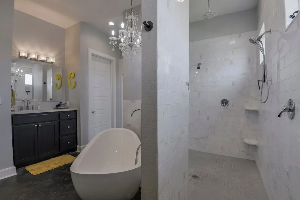 Spacious bathroom featuring a freestanding soaking tub, a walk-in shower with multiple showerheads and built-in shelving, a double vanity with ample storage, a decorative chandelier, and recessed lighting