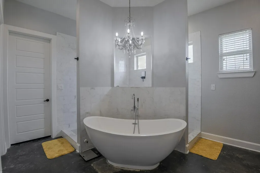 Freestanding soaking tub with a floor-mounted faucet, flanked by two walk-in shower enclosures with clear glass panels