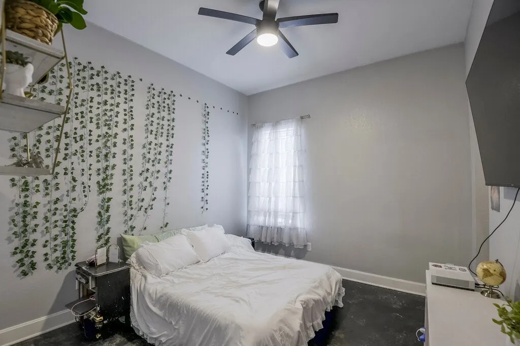 Bedroom featuring a ceiling fan with integrated lighting, a window with sheer curtains, and dark-finish flooring