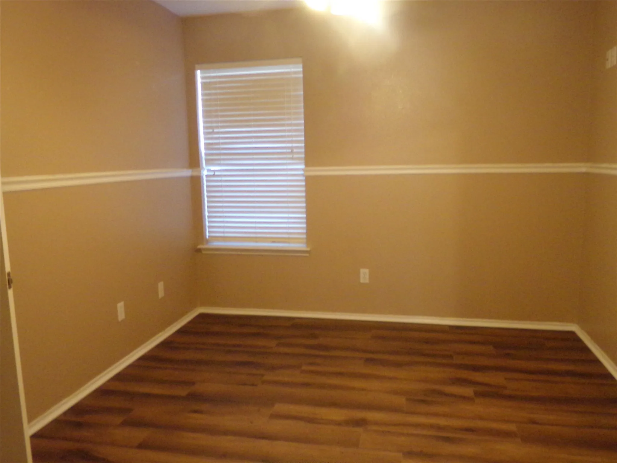 Room featuring wood-finish flooring, a window with blinds, and neutral-toned walls with decorative trim