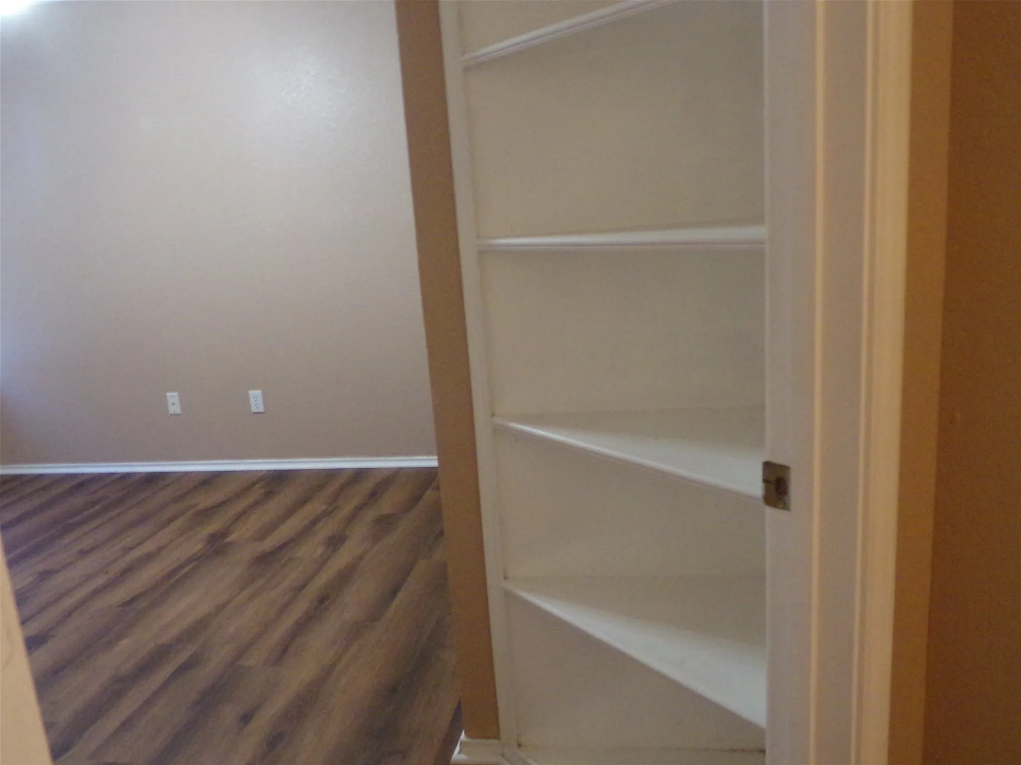 Built-in shelving unit with multiple white shelves, set against a neutral painted wall and wood-finish flooring