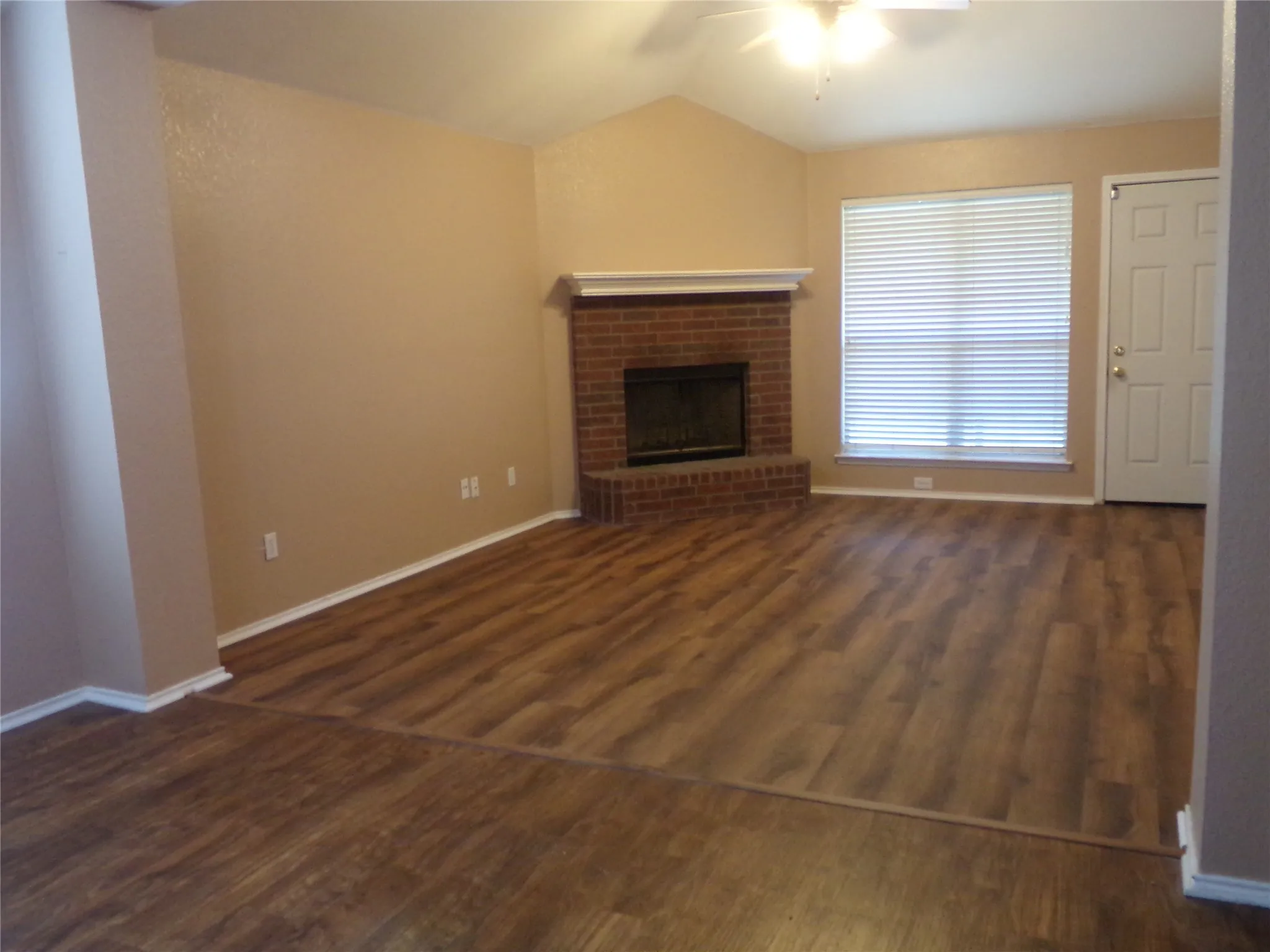 Living area featuring wood-finish flooring, a brick fireplace with a white mantel, and a vaulted ceiling with a ceiling fan