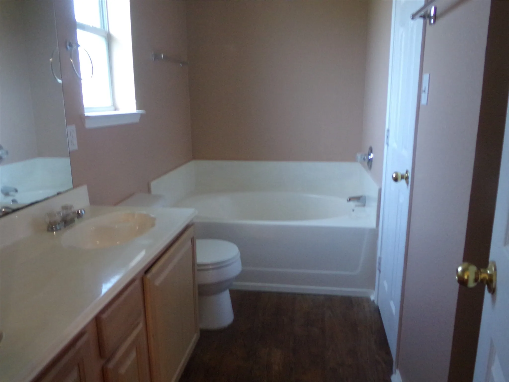 Bathroom featuring a single vanity with a built-in sink, light wood-finish cabinetry, and a full-size bathtub