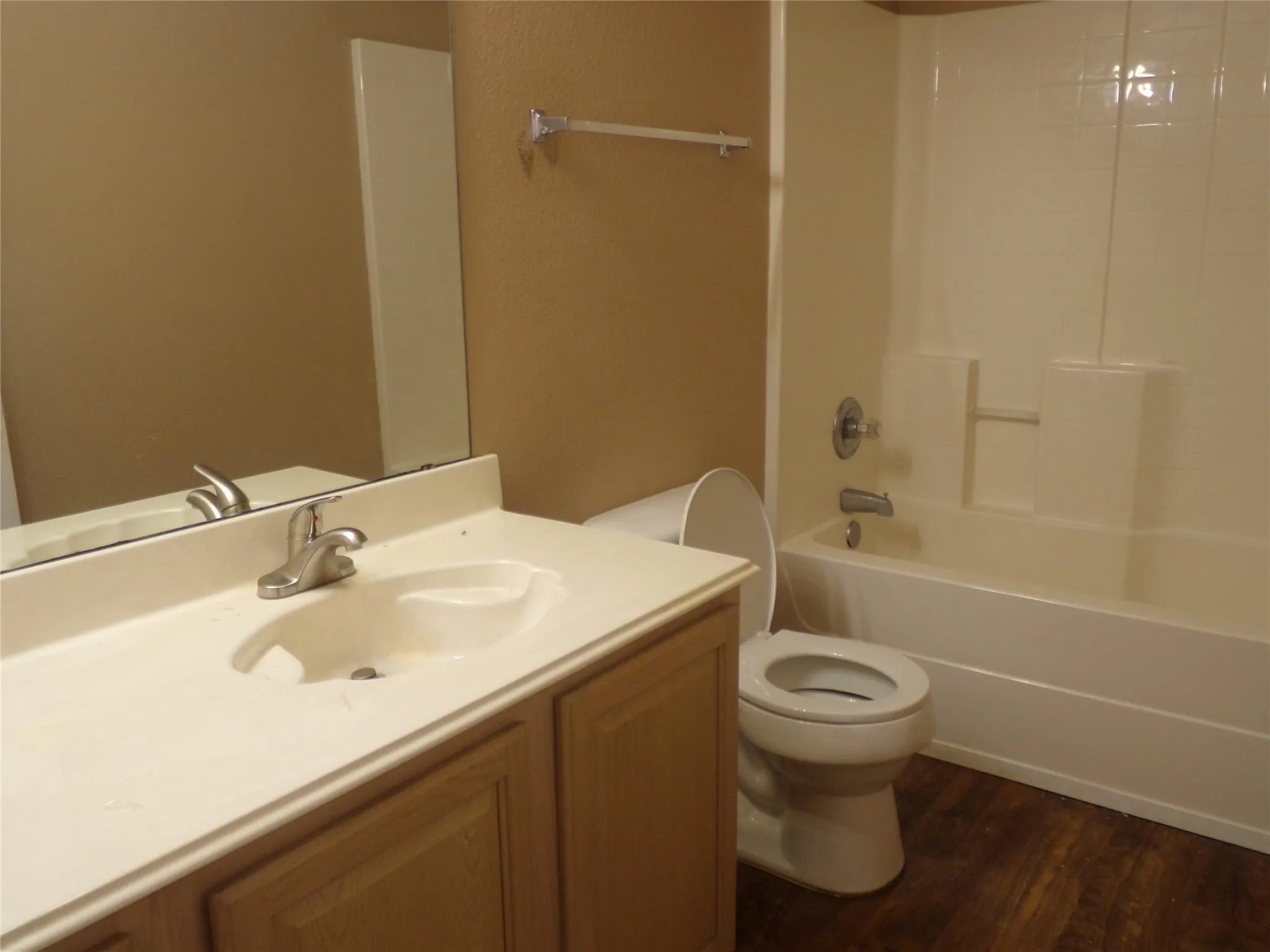 Hall Bathroom featuring wood-finish flooring, a vanity with a light-colored countertop and integrated sink, chrome-finish faucet, and a shower-tub combination with a white surround