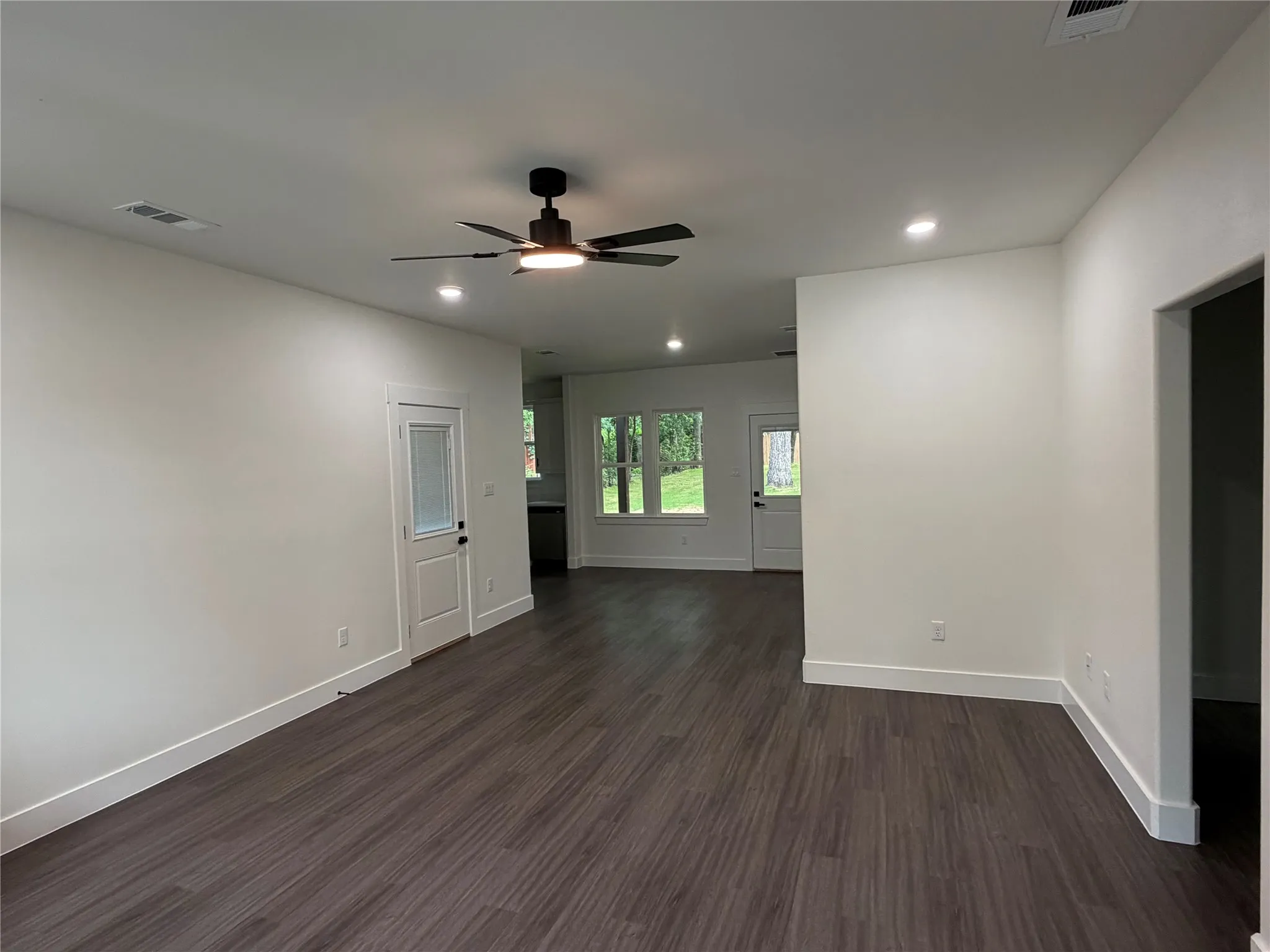 Spacious room featuring dark wood-finish flooring, white walls, and recessed lighting