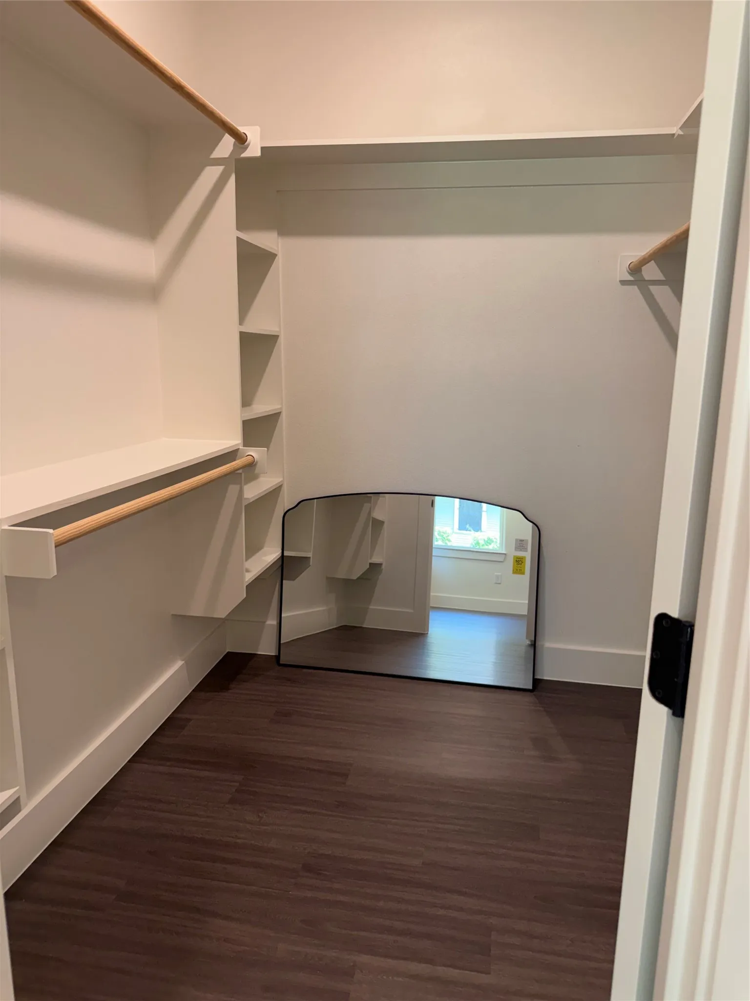 Walk-in closet featuring built-in shelving, two clothing rods, and dark wood-finish flooring