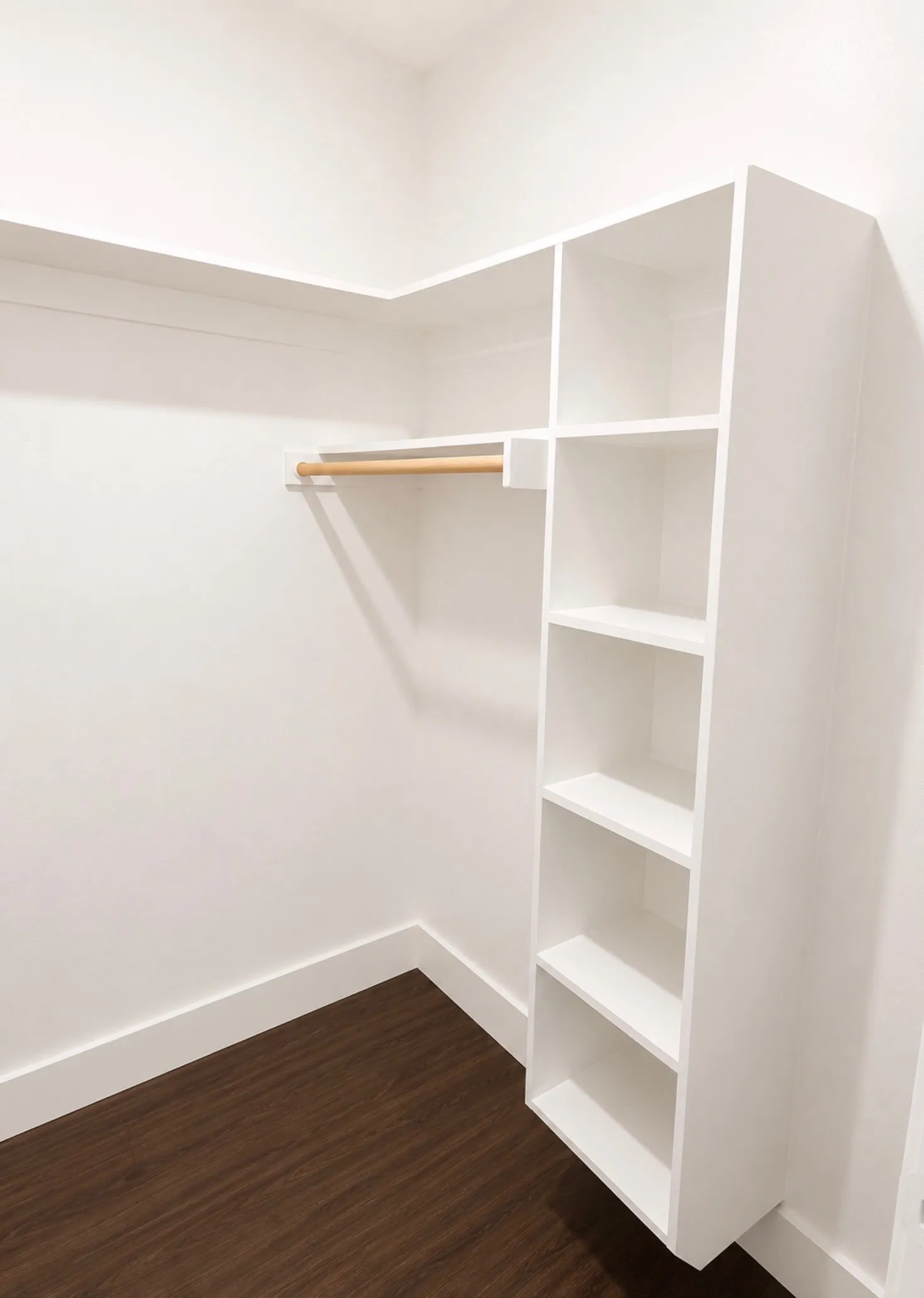Walk-in closet featuring built-in shelving, a natural wood hanging rod, crisp white walls, white baseboards, and dark wood-finish flooring