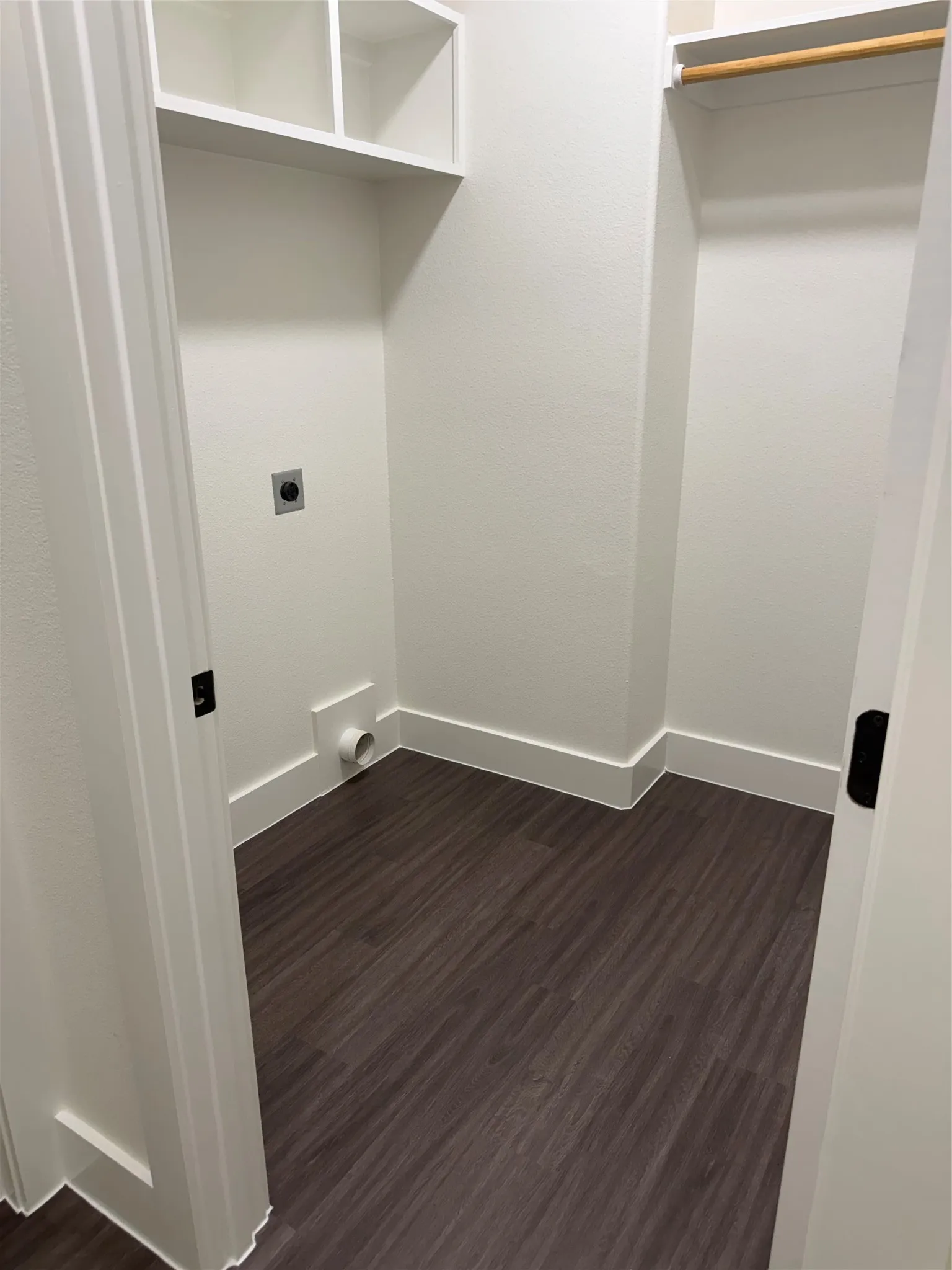 Dedicated laundry closet featuring wood-finish flooring, white baseboards, and built-in shelving
