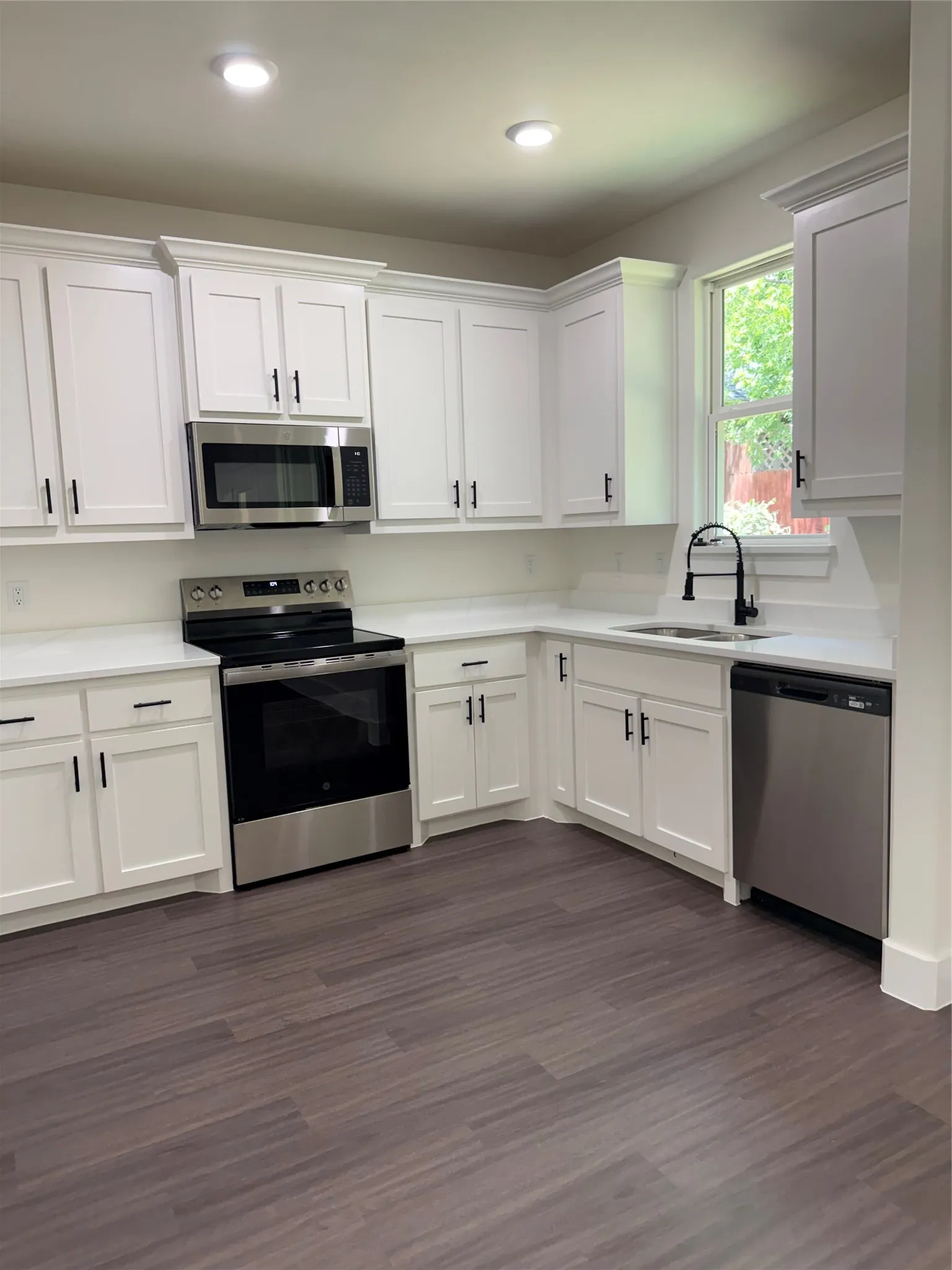 Modern kitchen featuring white shaker cabinetry with dark hardware, stainless steel appliances, and wood-finish flooring