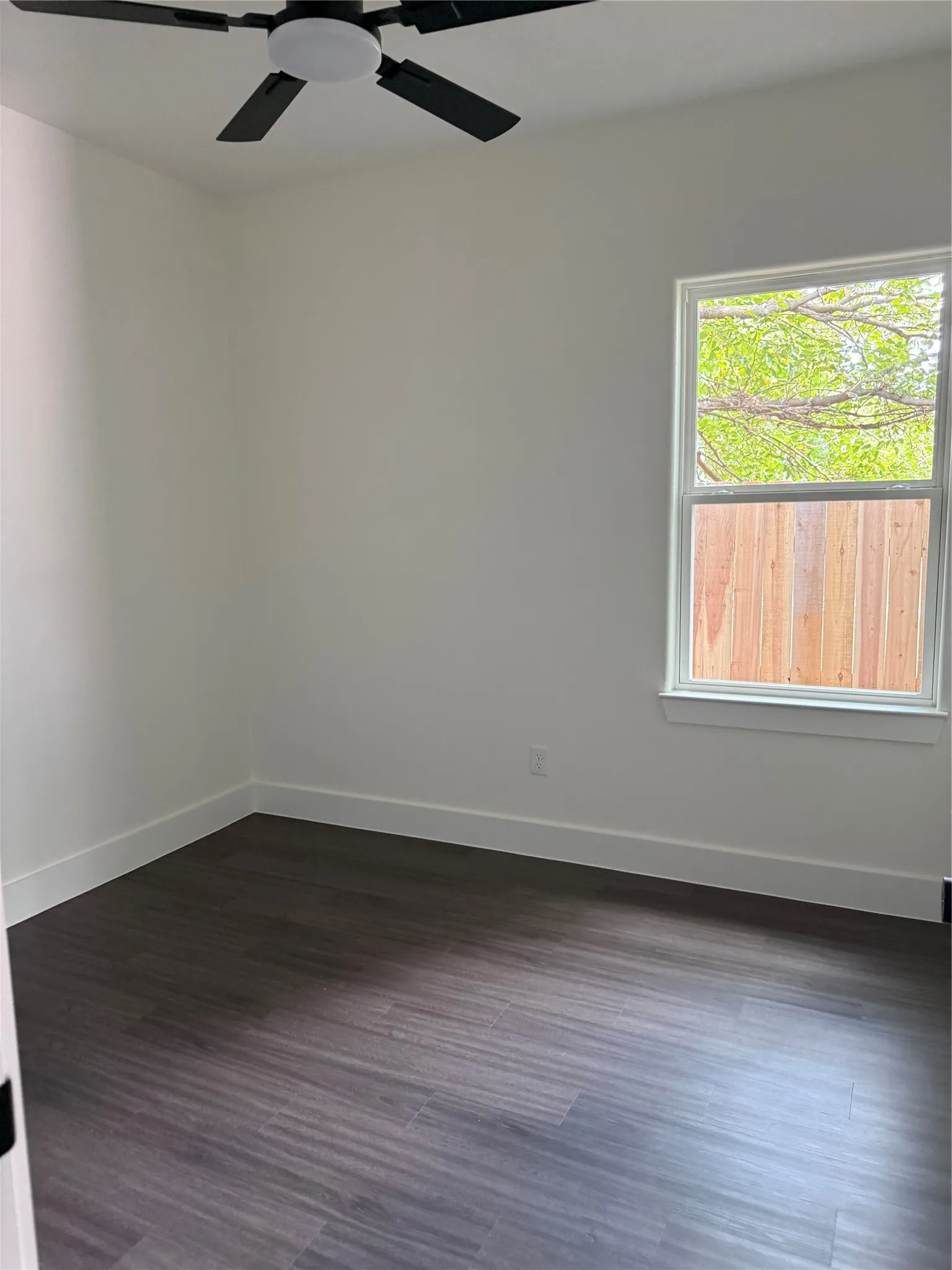 Interior space featuring wood-finish flooring, white baseboards, and a contemporary ceiling fan with integrated lighting