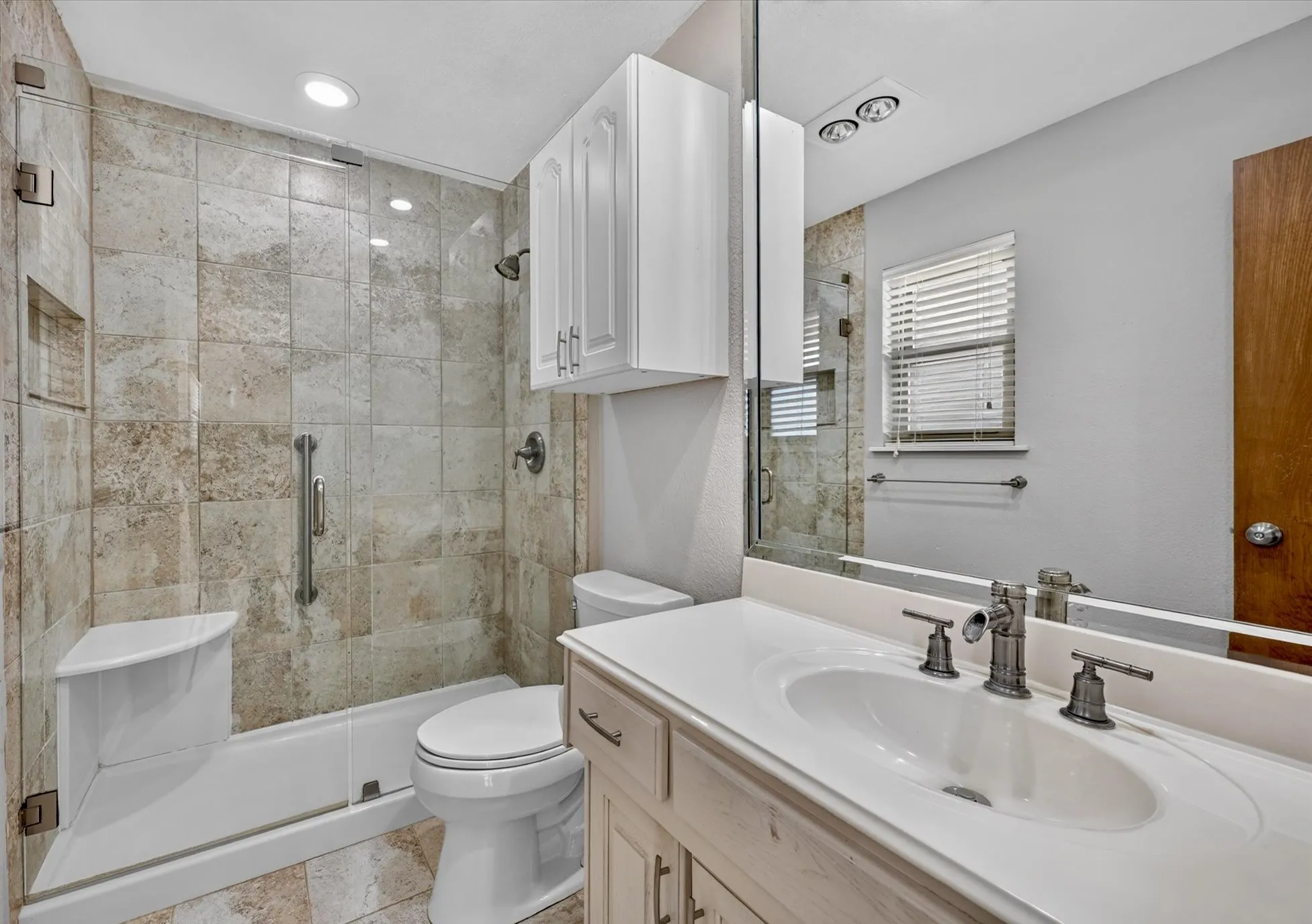 Updated primary bath featuring an oversized walk-in shower, custom tile, and abundant storage