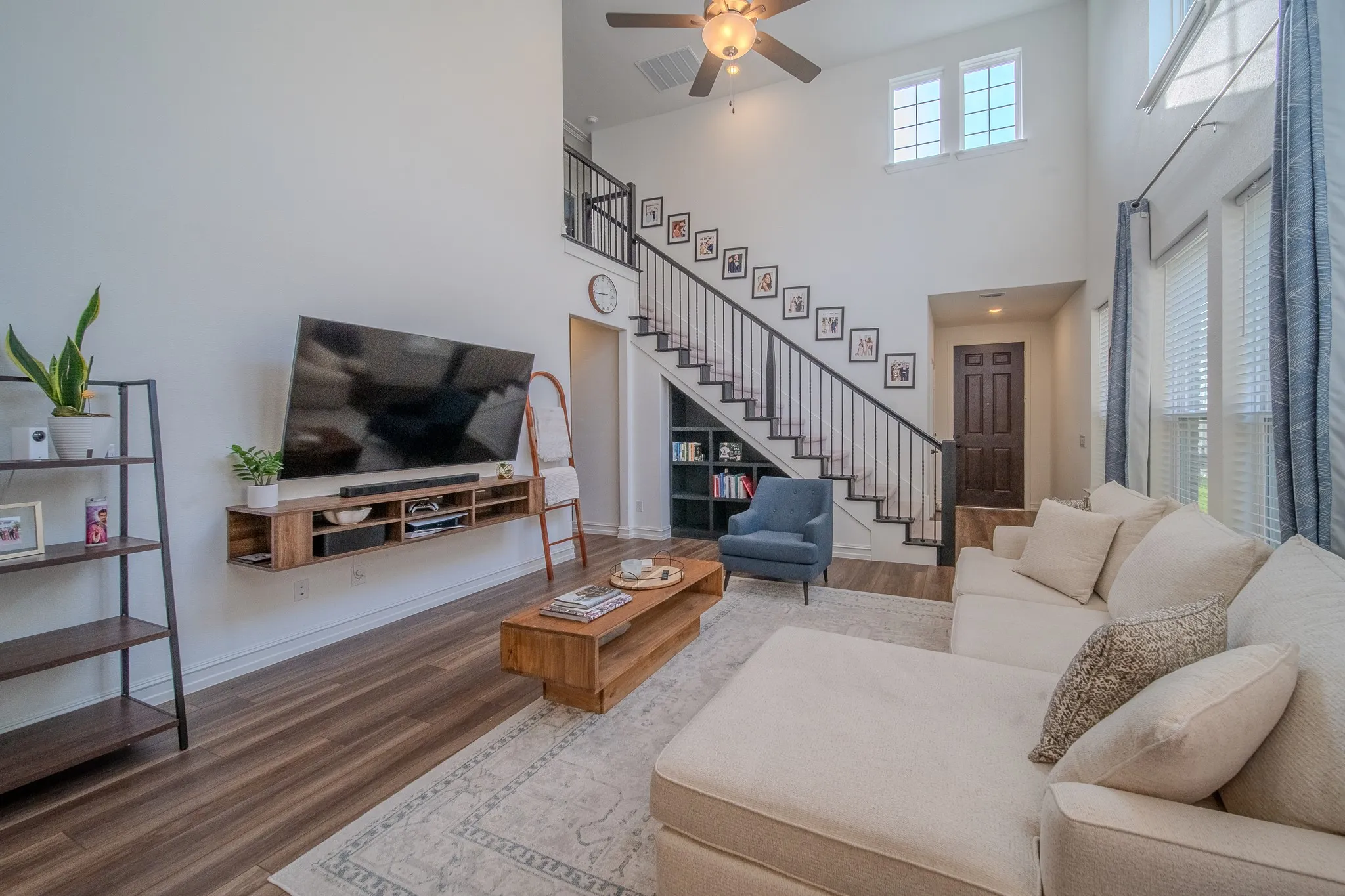 Two-story living area featuring wood-finish flooring, a contemporary floating media console, and a dark wood paneled door