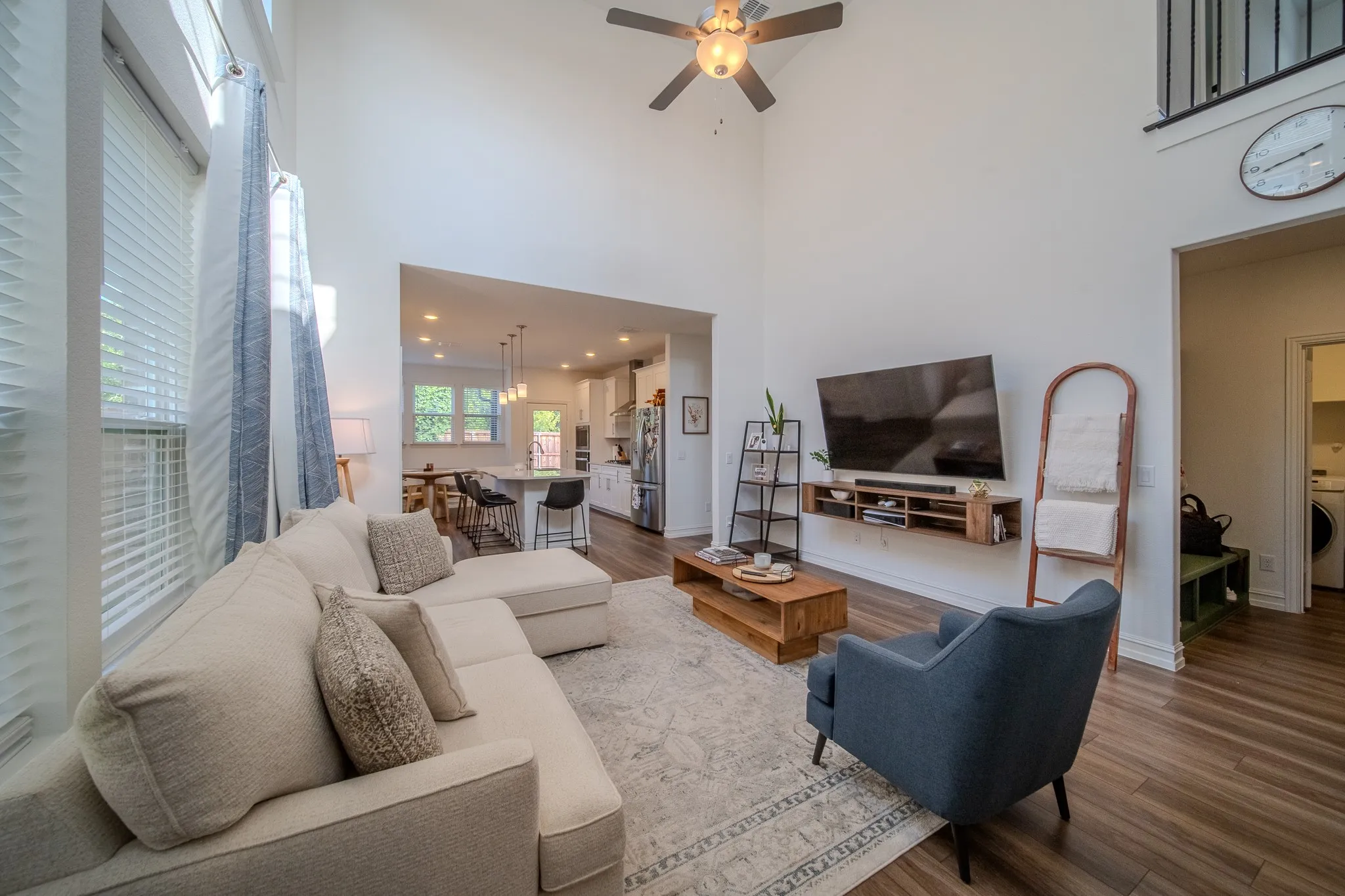 Vaulted ceilings enhance this open-concept living area featuring wood-finish flooring, a contemporary ceiling fan, and abundant natural light from tall windows