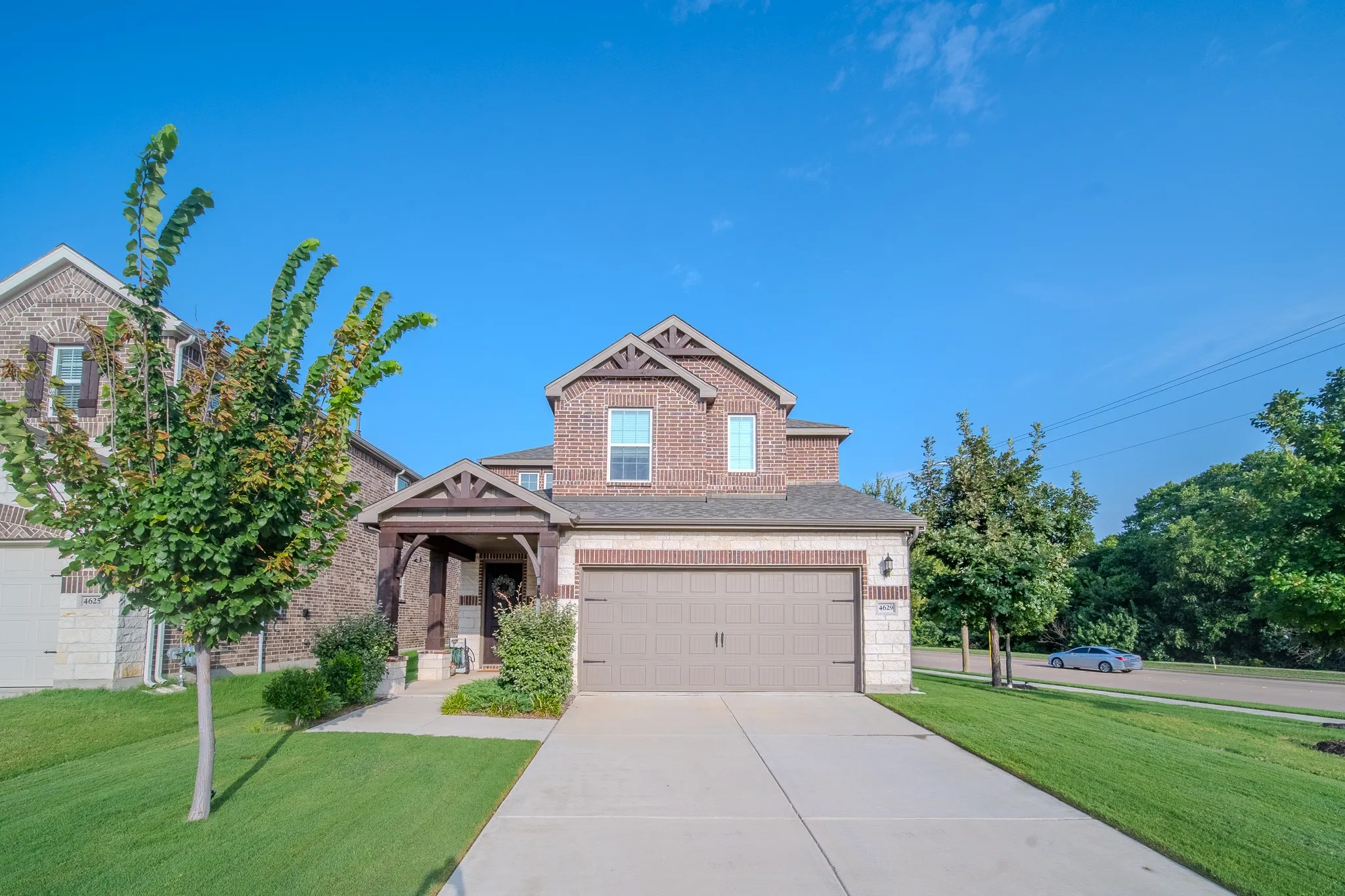 Two-story residence featuring brick and stone veneer, a covered entry with timber-style accents, and an attached two-car garage