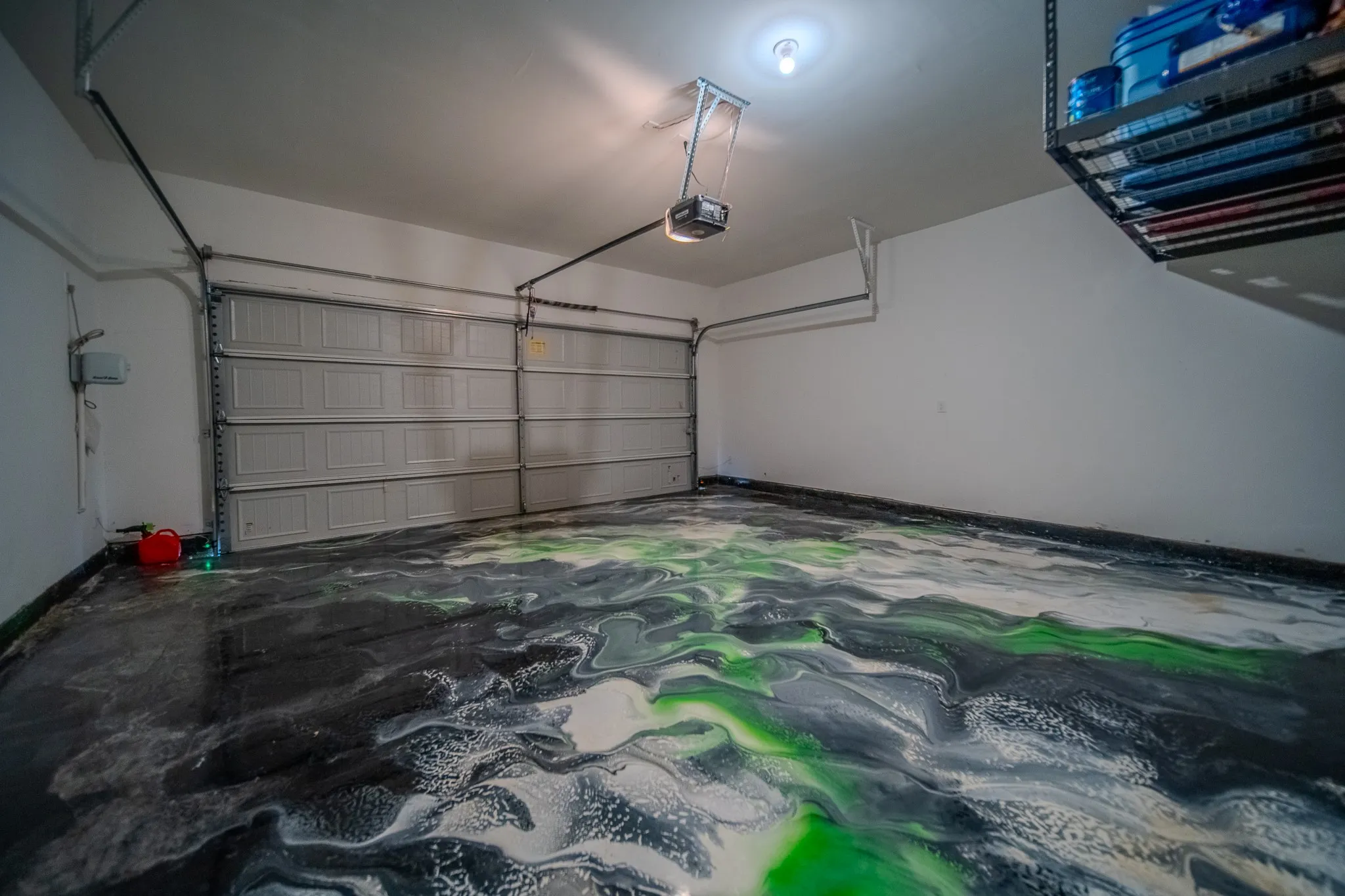 Garage featuring a distinctive multi-color epoxy floor, overhead storage rack, and automatic garage door opener