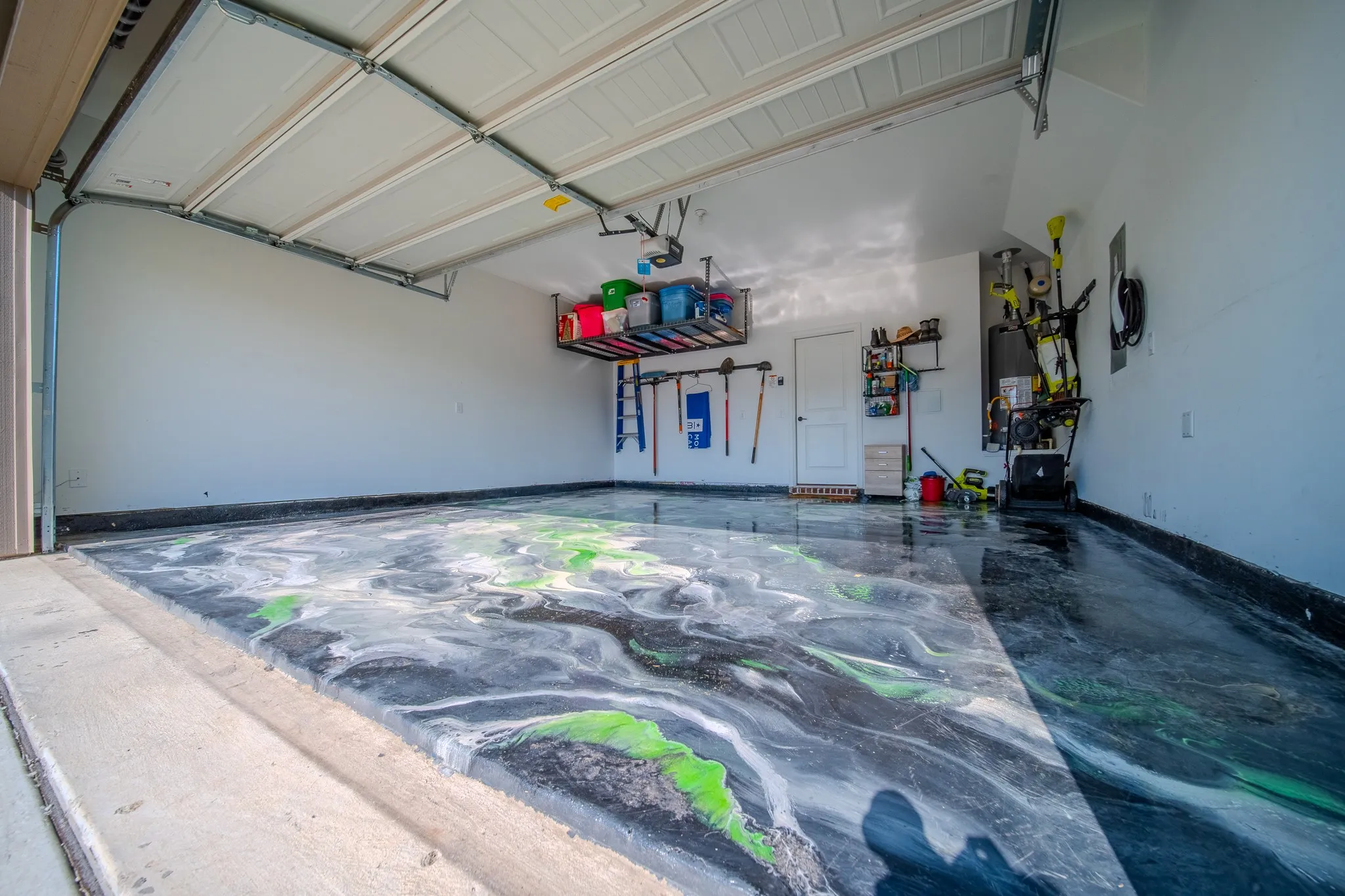 Interior garage featuring a custom epoxy floor, white walls, and an overhead storage rack