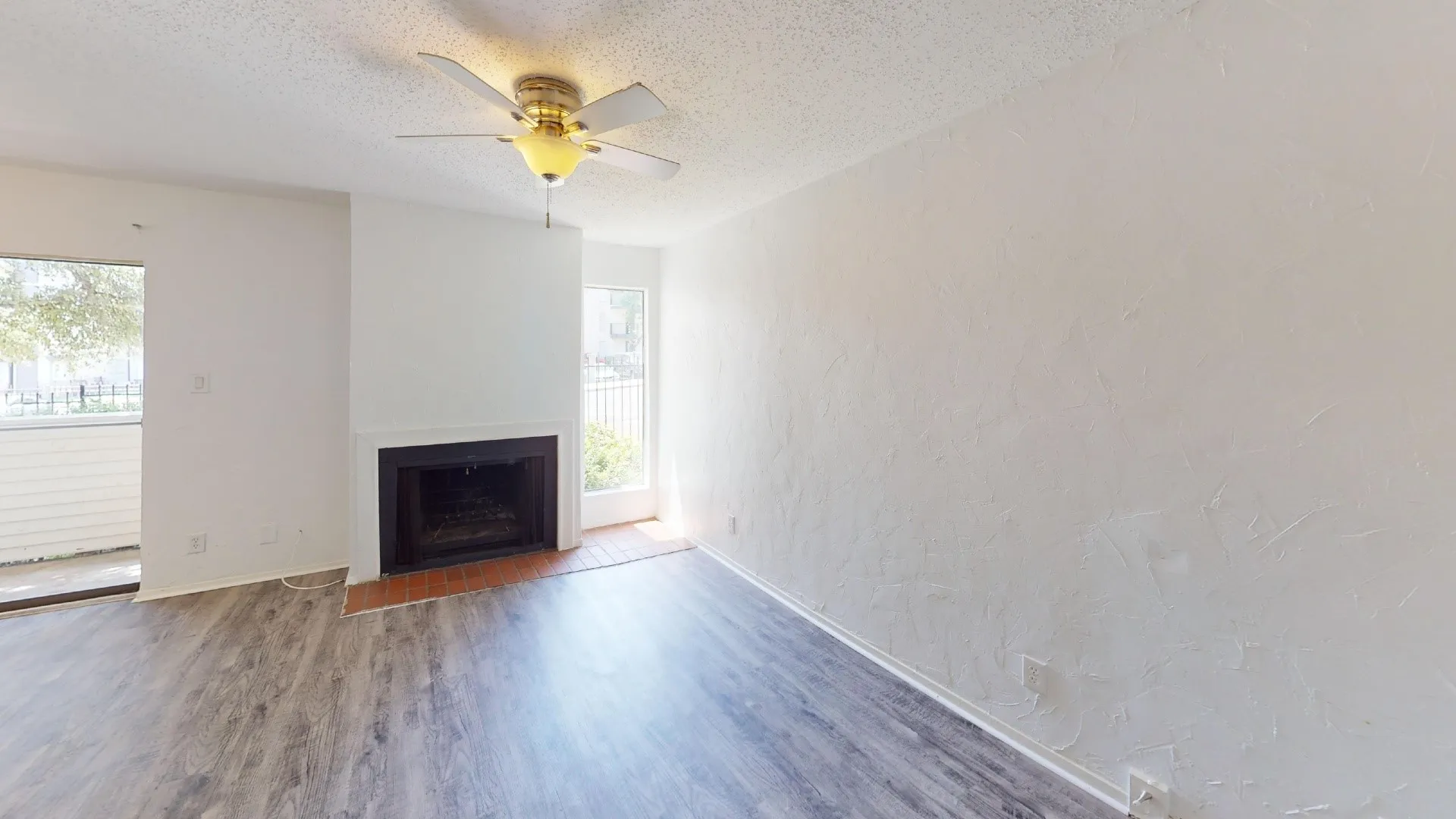 Living area featuring wood-finish flooring, a fireplace with a brick hearth, a ceiling fan with integrated lighting, and white textured walls