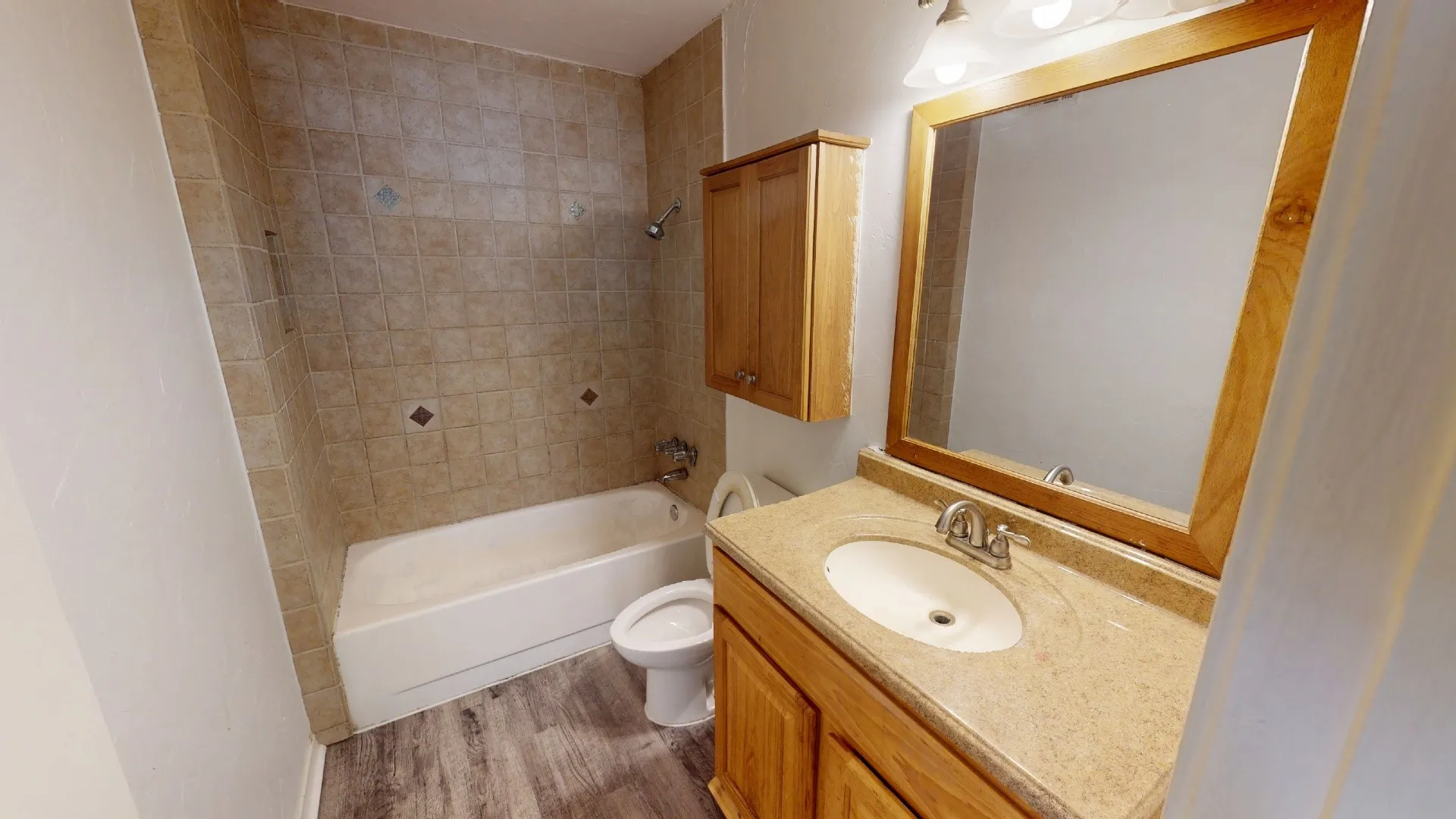 Bathroom featuring a tiled shower and tub combination, a vanity with an integrated sink and stone-finish countertop, a wooden framed mirror, and wood-finish flooring