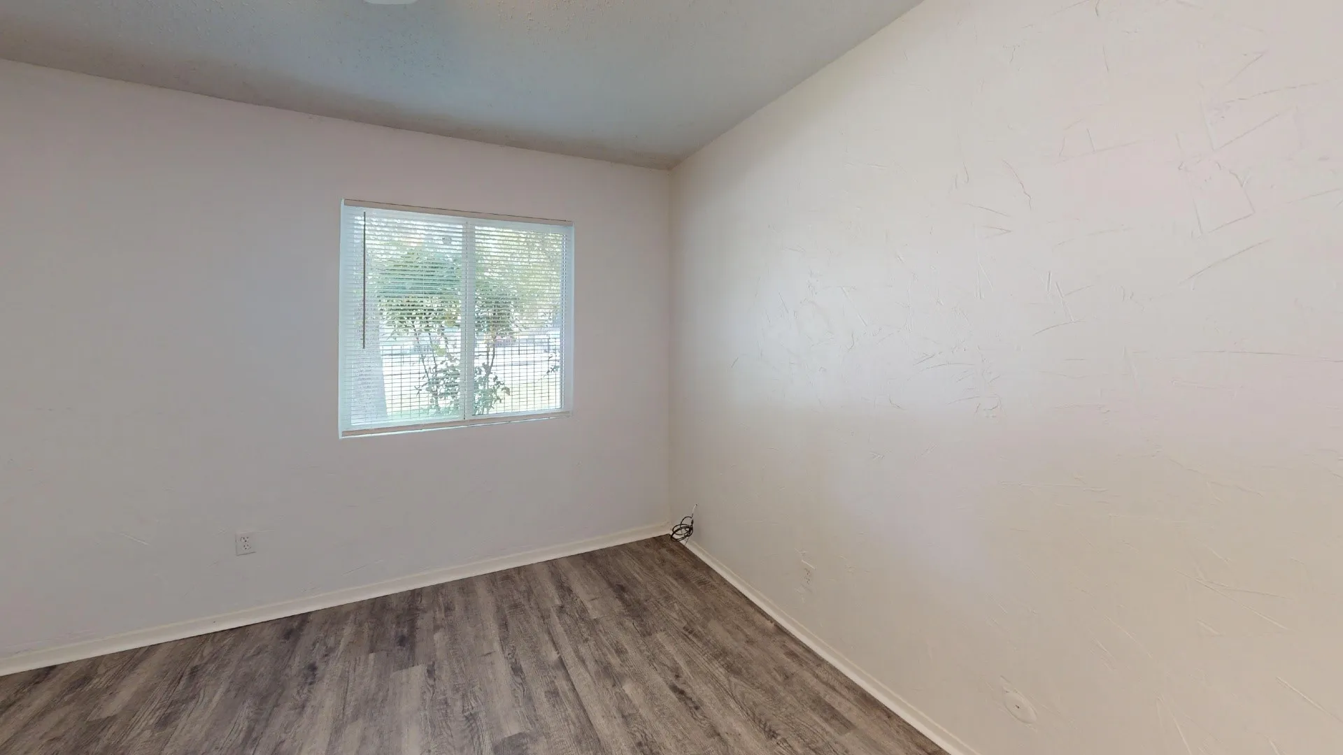 Spacious room featuring wood-finish flooring, white baseboards, and neutral wall tones