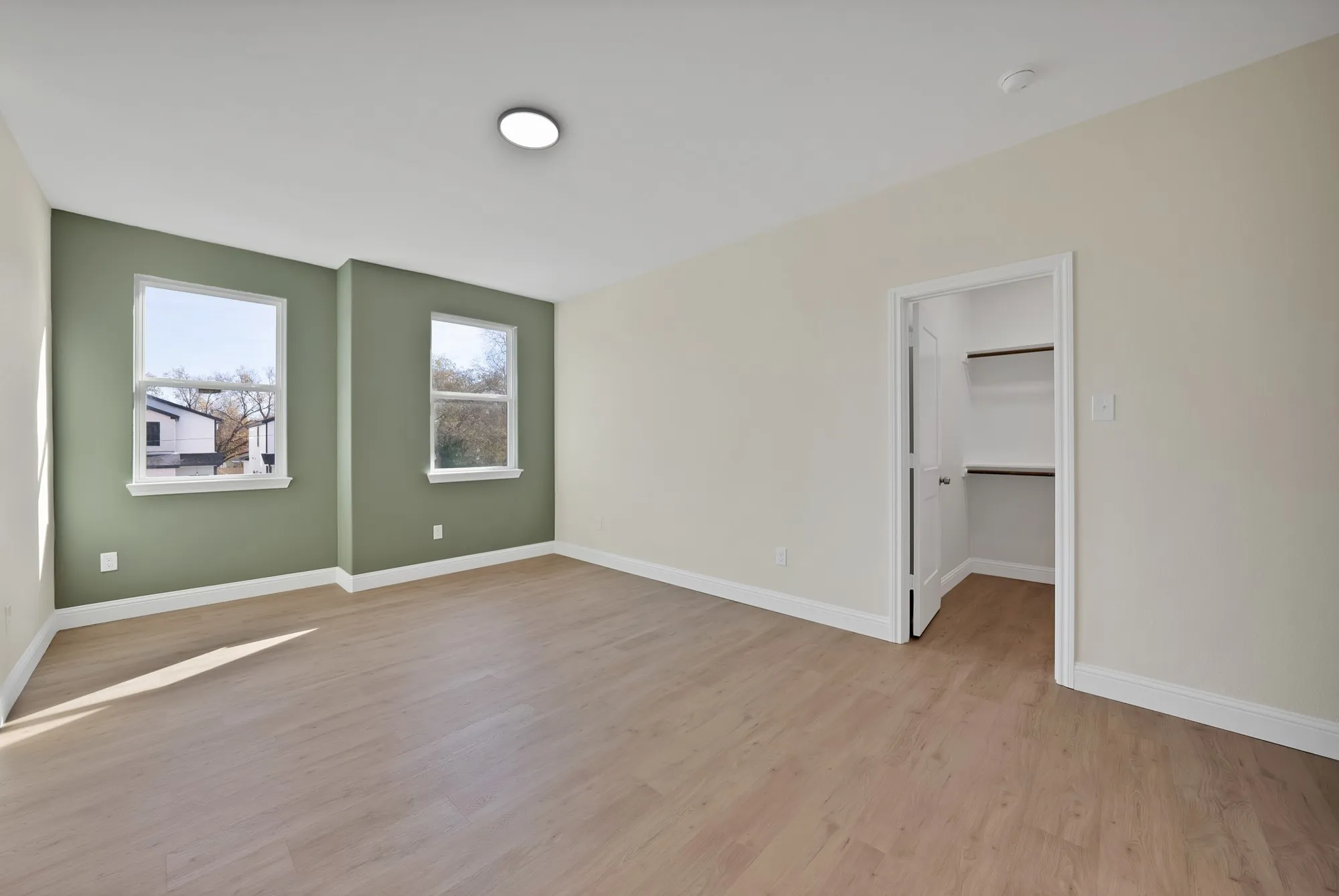 Spacious room featuring wood-finish flooring, two large windows with white trim, a recessed ceiling light, and an open closet with built-in shelving