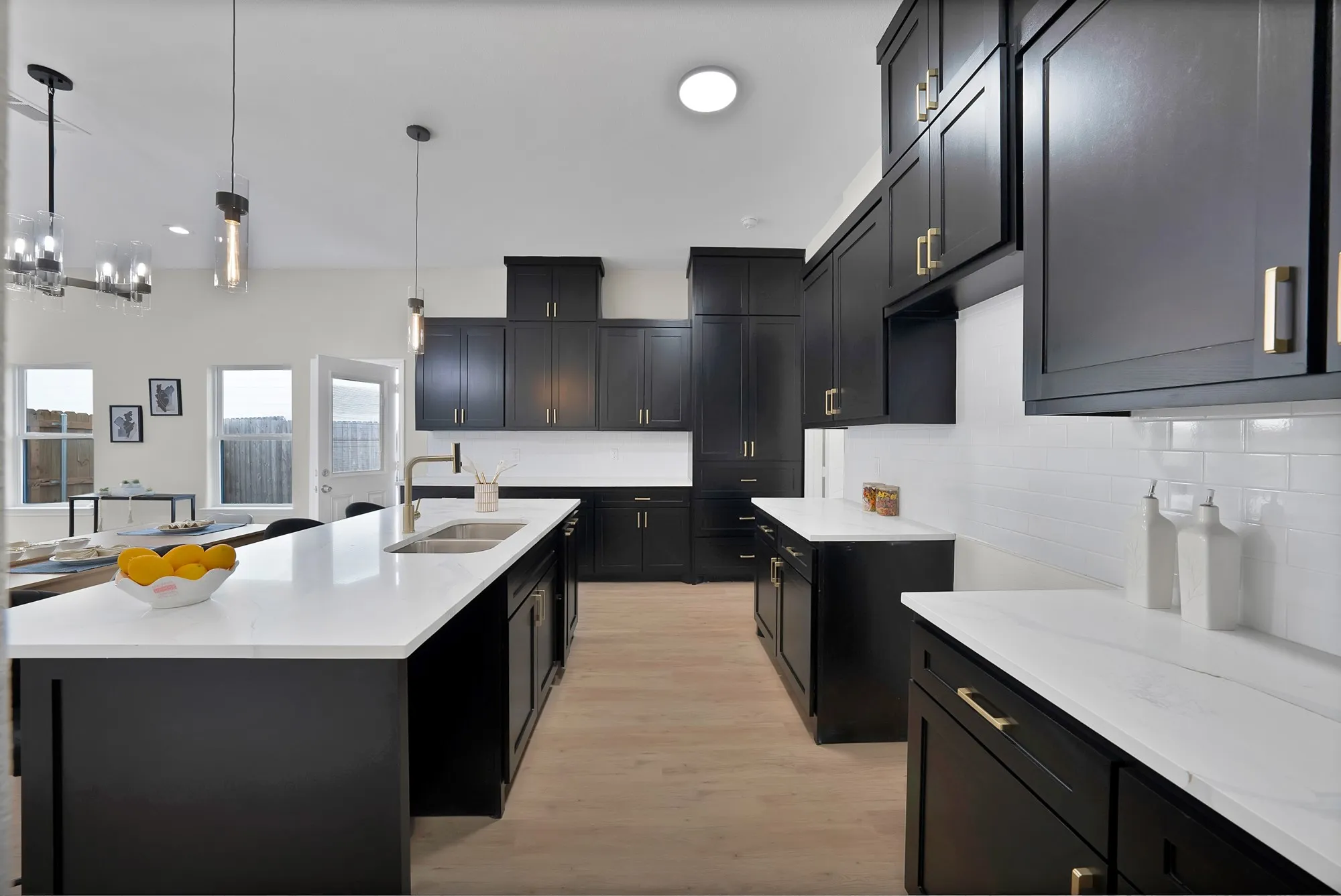 Spacious kitchen featuring dark cabinetry with gold-toned hardware, extensive white countertops, and a subway tile backsplash