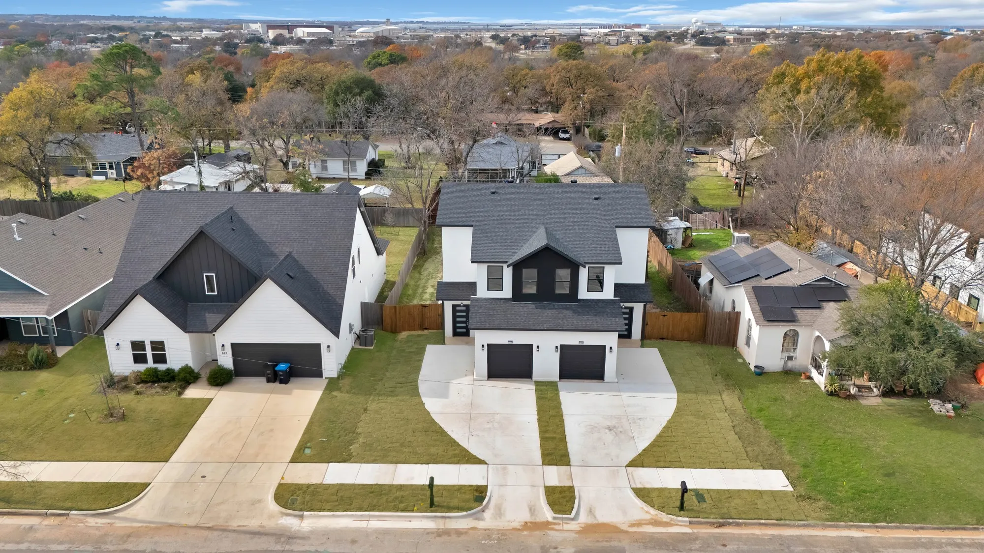 Modern duplex featuring white exteriors with black trim, a dark shingle roof, and a two-car garage for each unit