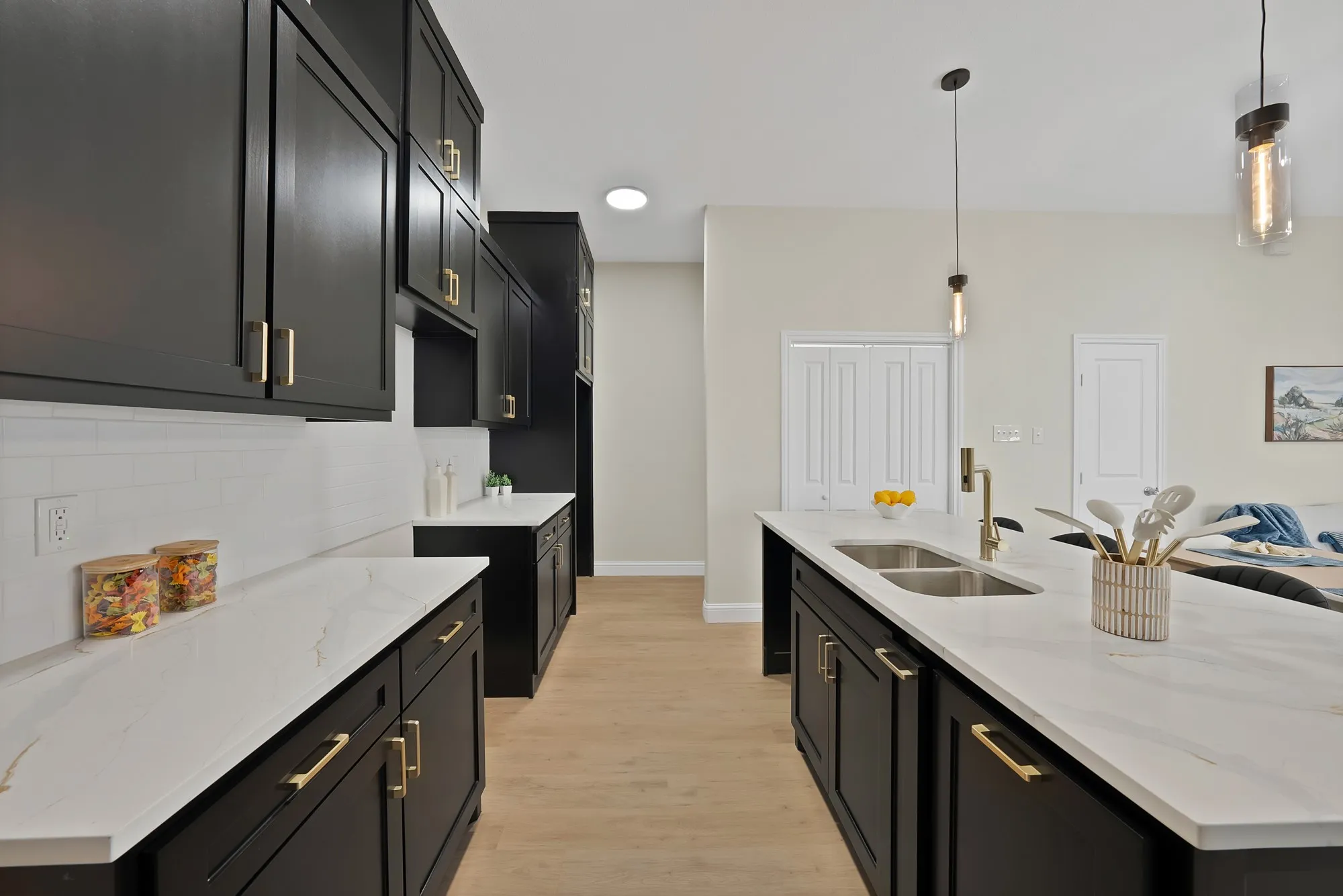 Kitchen featuring dark cabinetry with gold-finish hardware, white countertops, white subway tile backsplash, and light wood-finish flooring