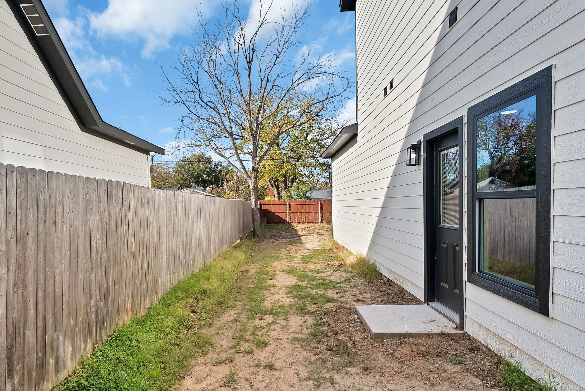Side yard featuring a privacy fence, mature deciduous tree, and a concrete patio pad