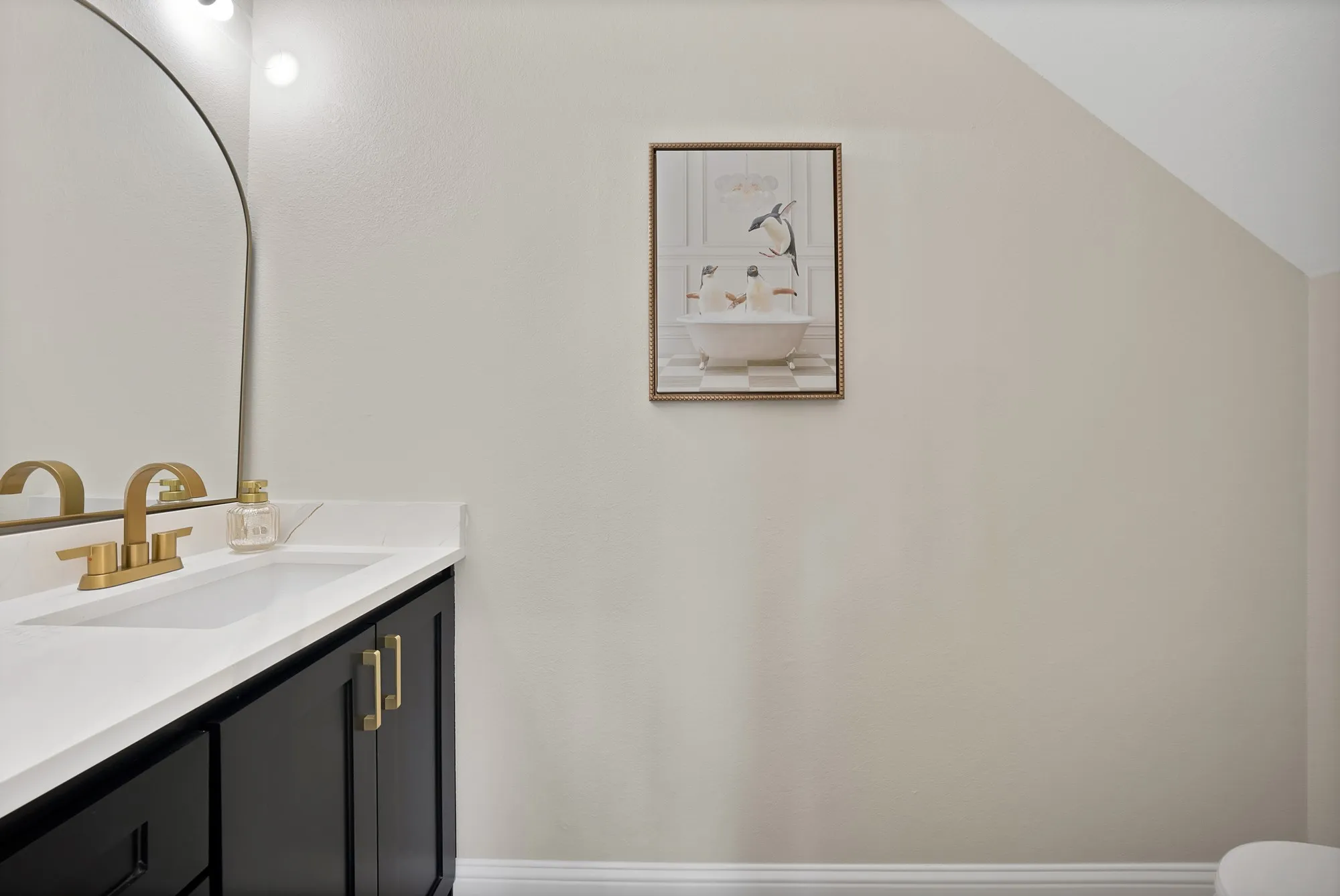Vanity featuring a white countertop with integrated sink, black cabinetry, and gold-finish hardware