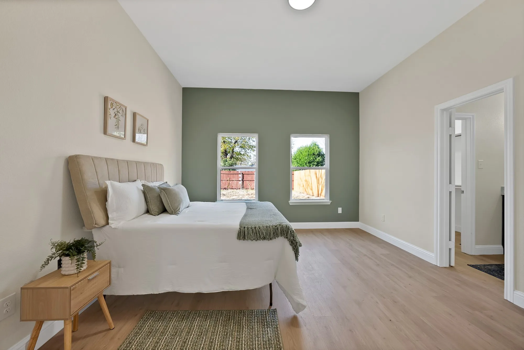 Spacious room featuring light wood-finish flooring, a contemporary accent wall, two windows with white trim, and a high ceiling