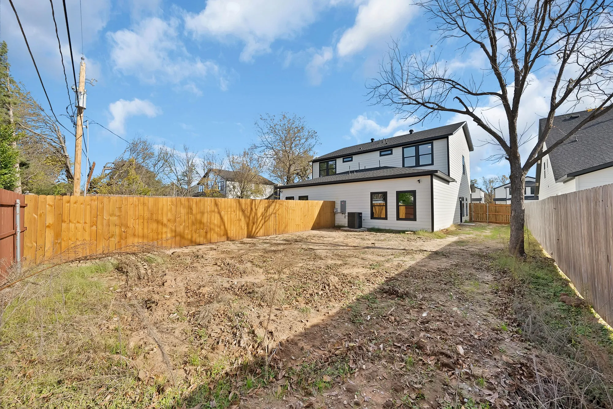 Spacious backyard featuring a new wood privacy fence, a newly constructed residence with white siding and black-framed windows, and ample open ground for landscaping