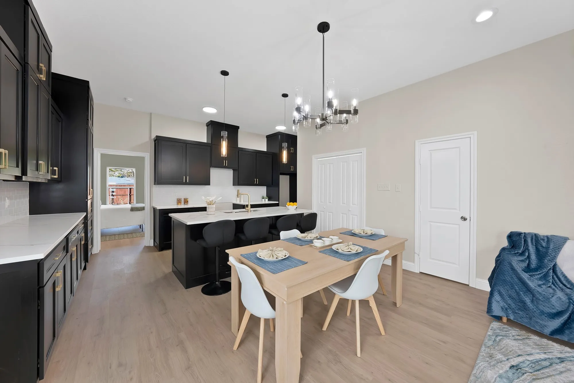 Open-concept kitchen and dining area featuring dark cabinetry with gold-toned hardware, light countertops, and a central island with pendant lighting